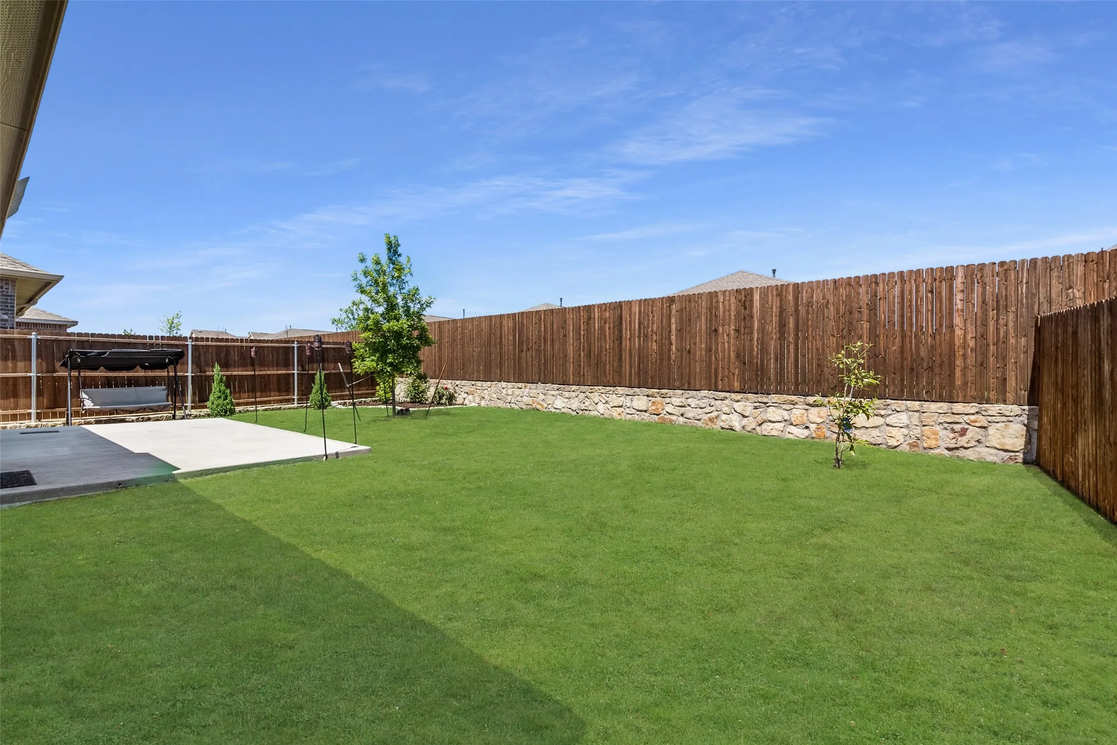 Expansive backyard featuring a manicured lawn, stone retaining wall, and wood privacy fencing