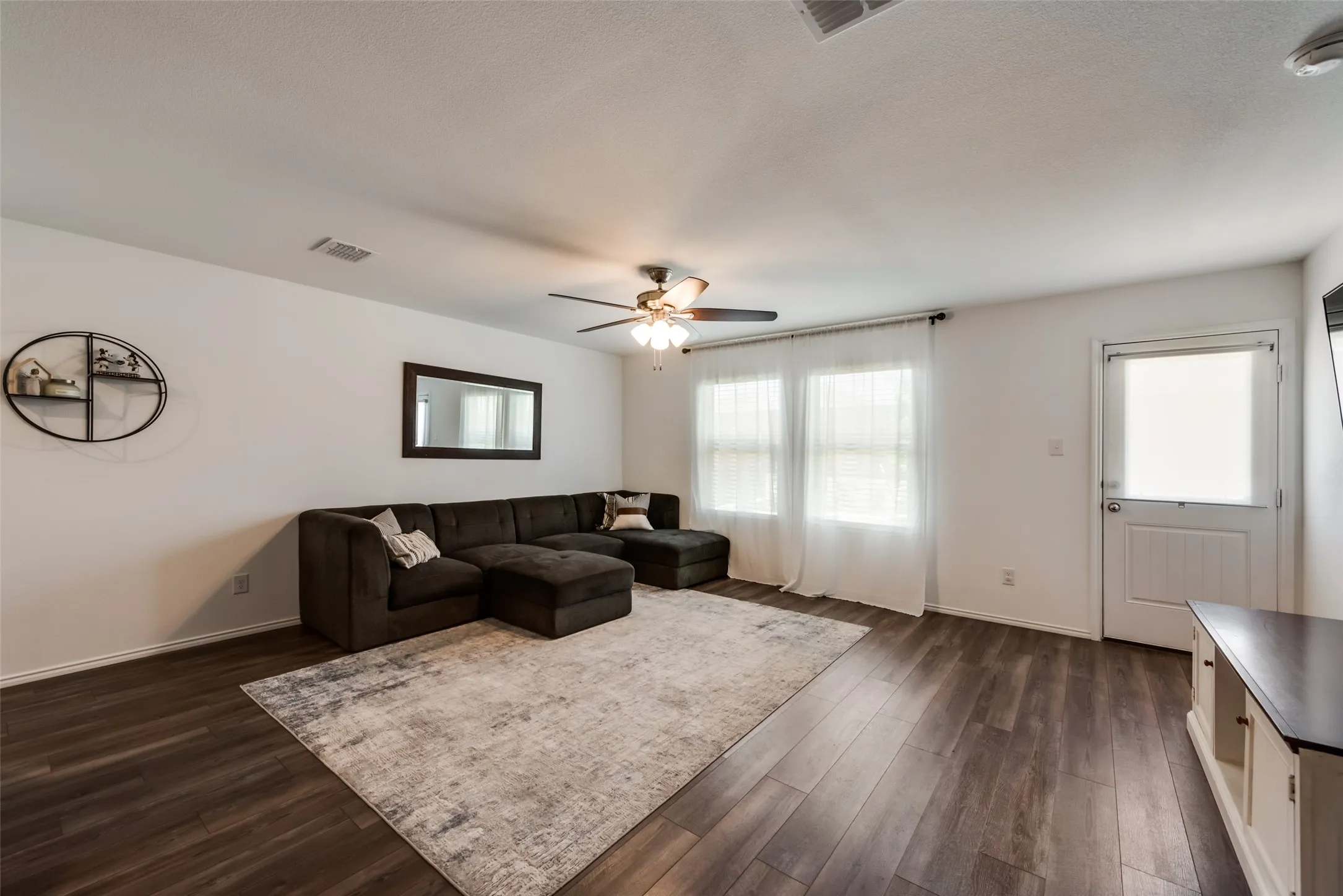 White walls featuring wood-finish flooring, a ceiling fan with integrated lighting, and multiple windows with curtain rods