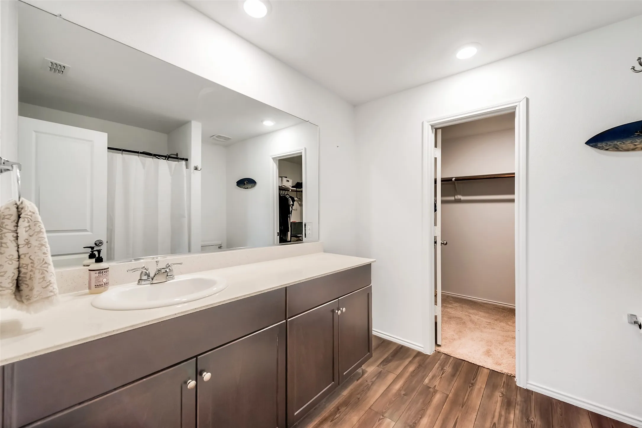 Bathroom featuring a wood-finish floor, a vanity with a light-colored countertop and undermount sink, dark cabinetry with silver hardware, and a large wall-mounted mirror