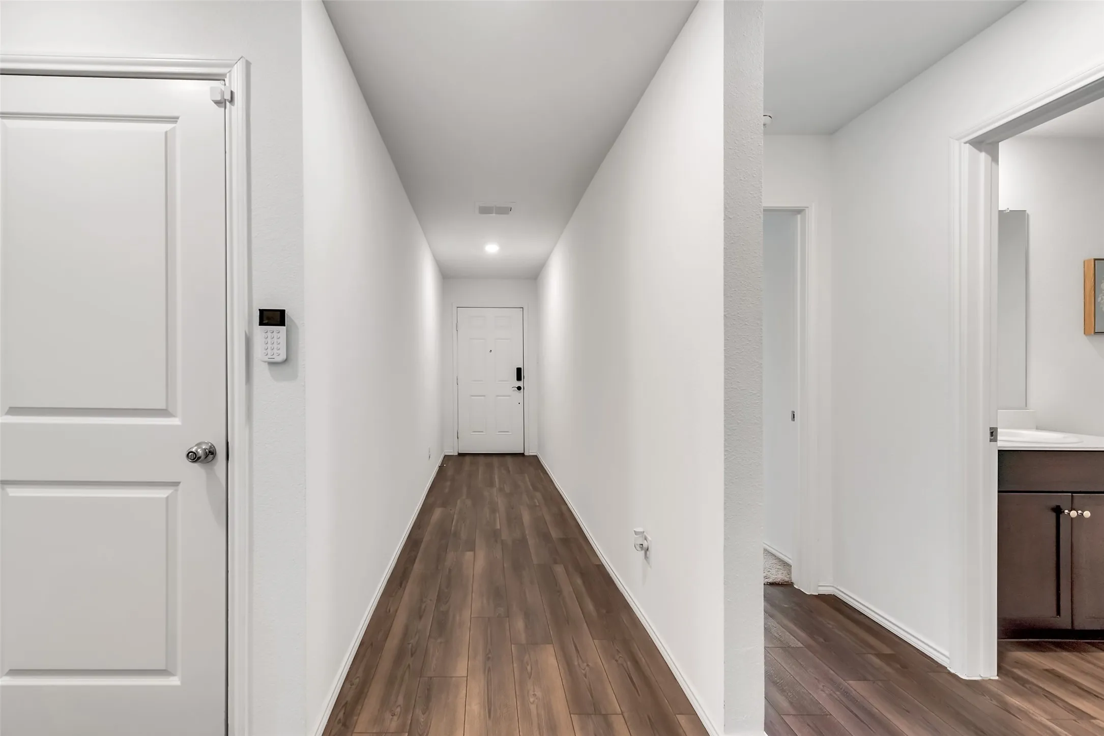 White interior doors, wood-finish flooring, recessed lighting, white walls, and a built-in vanity with dark cabinetry