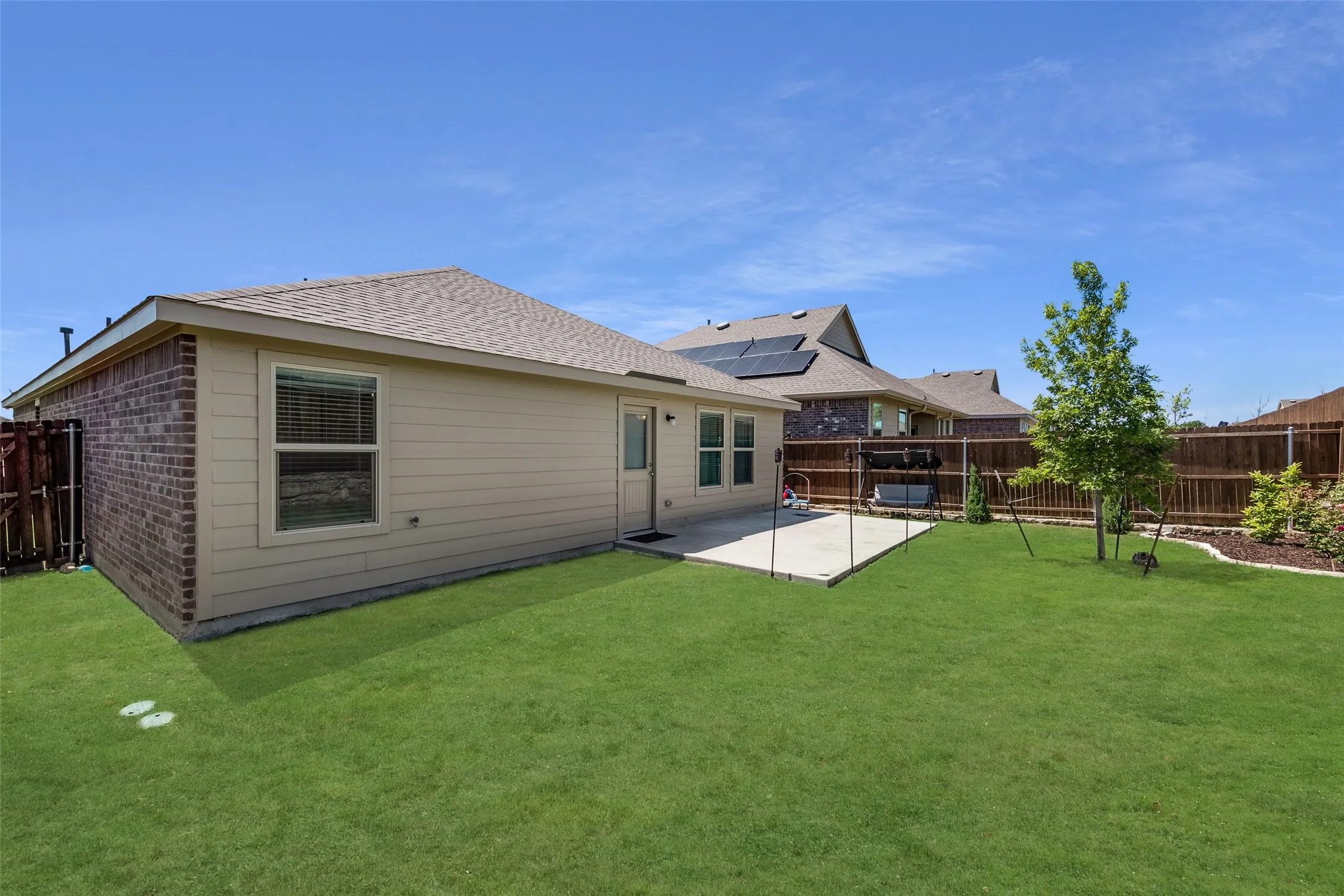 Expansive backyard with a concrete patio, wood fencing, and a mature tree