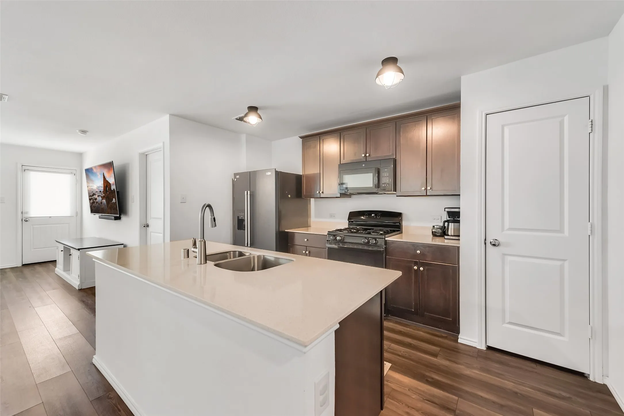 Kitchen featuring a central island with an undermount double sink, dark wood-finish cabinetry, stainless steel appliances, and wood-finish flooring