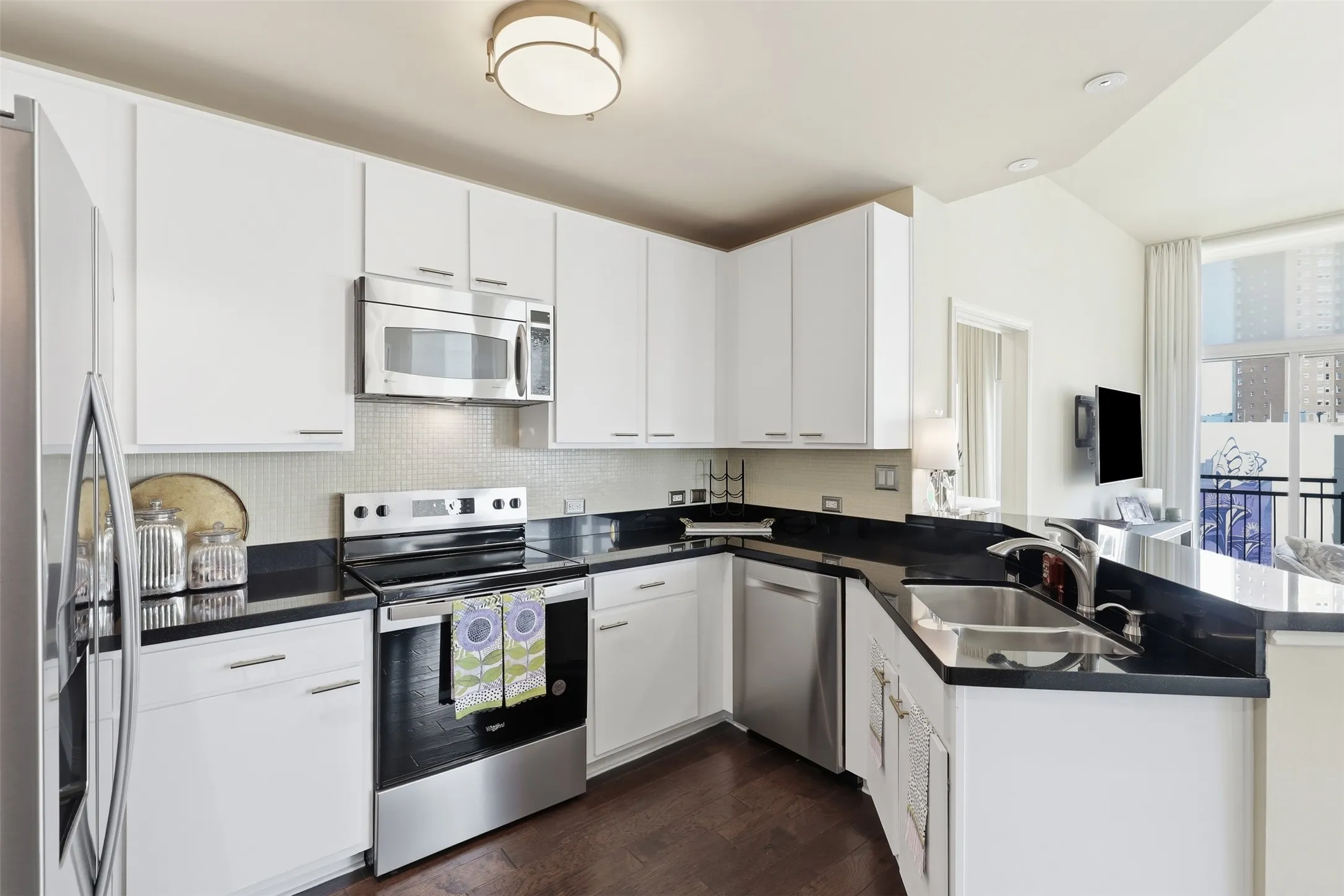 White cabinetry with brushed nickel hardware, dark countertops, stainless steel appliances, and a stainless steel sink with a single-handle faucet