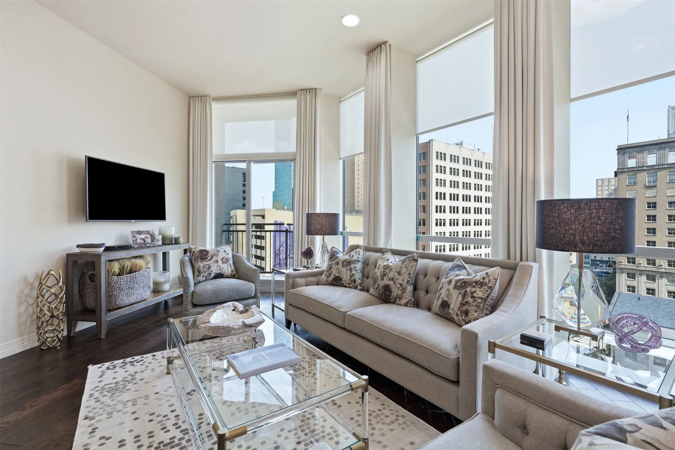 Expansive floor-to-ceiling windows with roller shades, dark wood-finish flooring, and a glass sliding door leading to an outdoor balcony