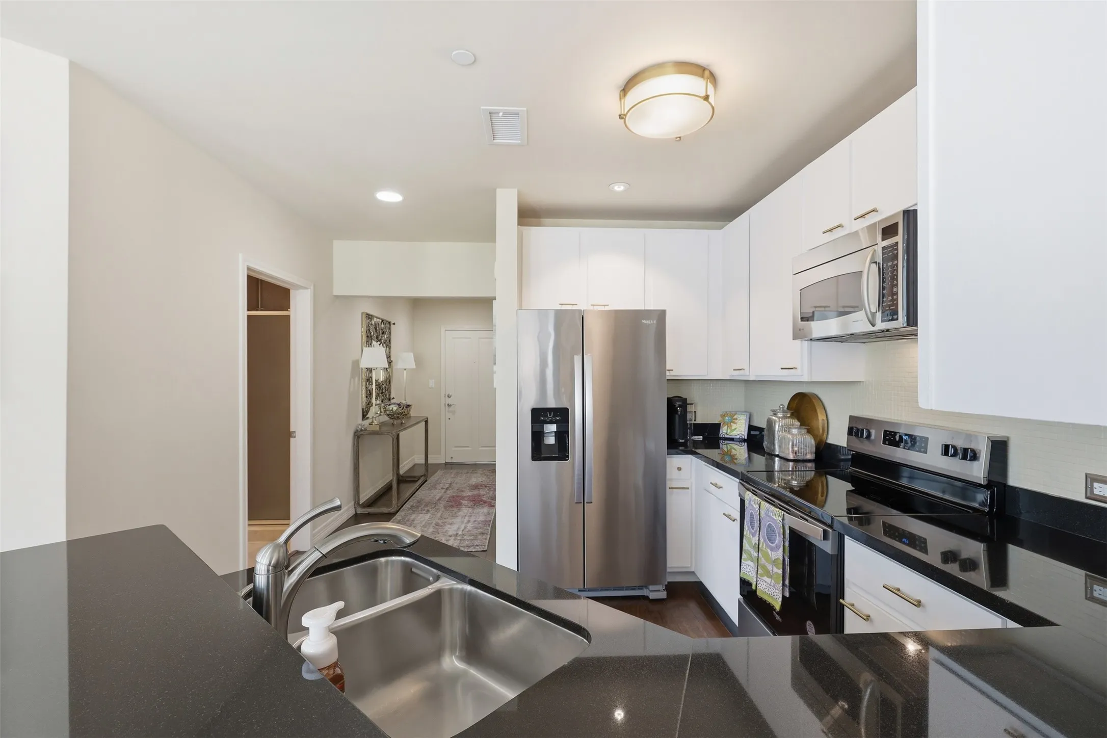 Kitchen featuring stainless steel appliances, dark countertops, white cabinetry, a double basin sink, and recessed lighting