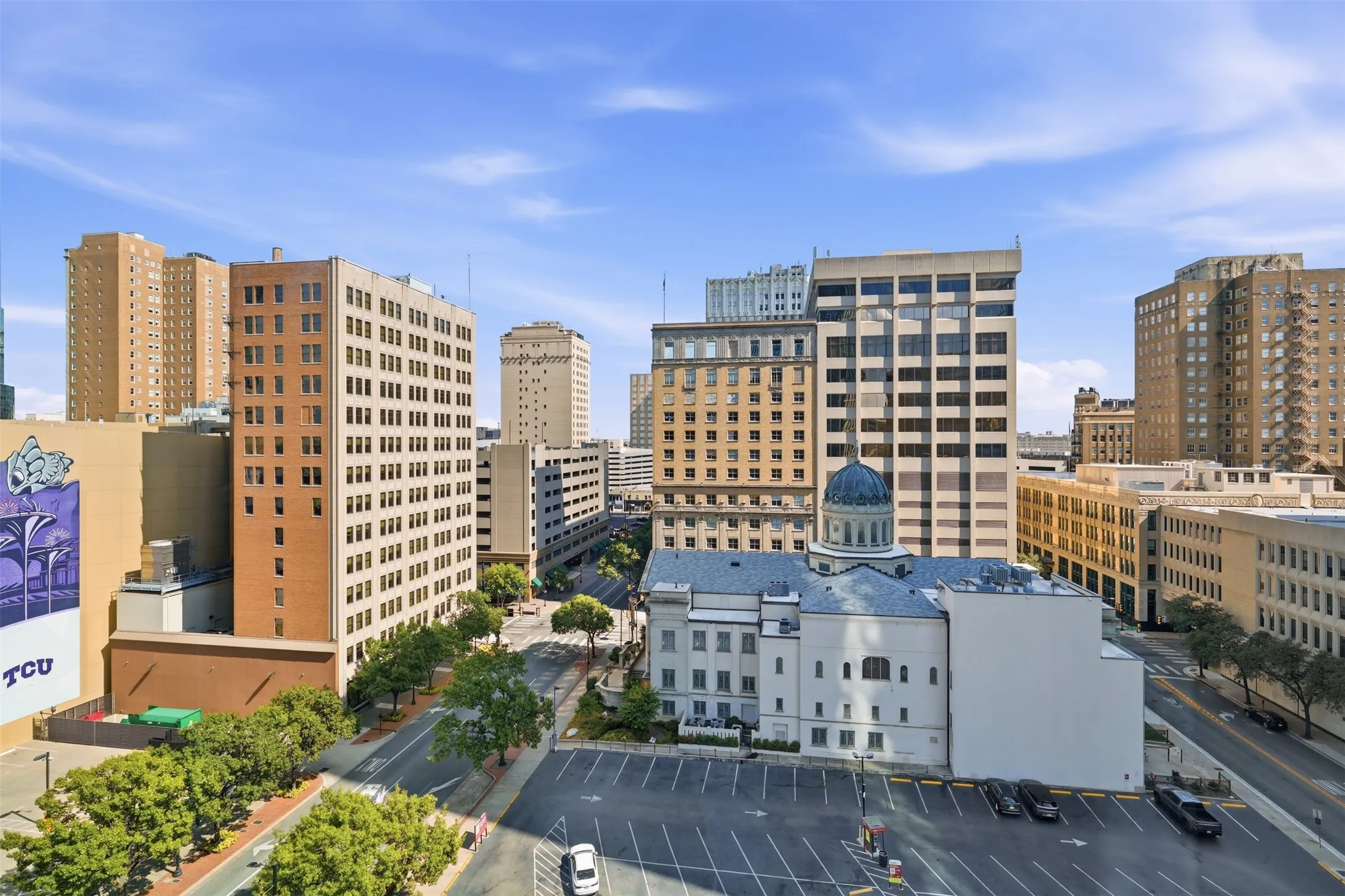 Urban cityscape featuring multiple high-rise buildings, an historic building with a blue dome, and paved streets lined with mature trees