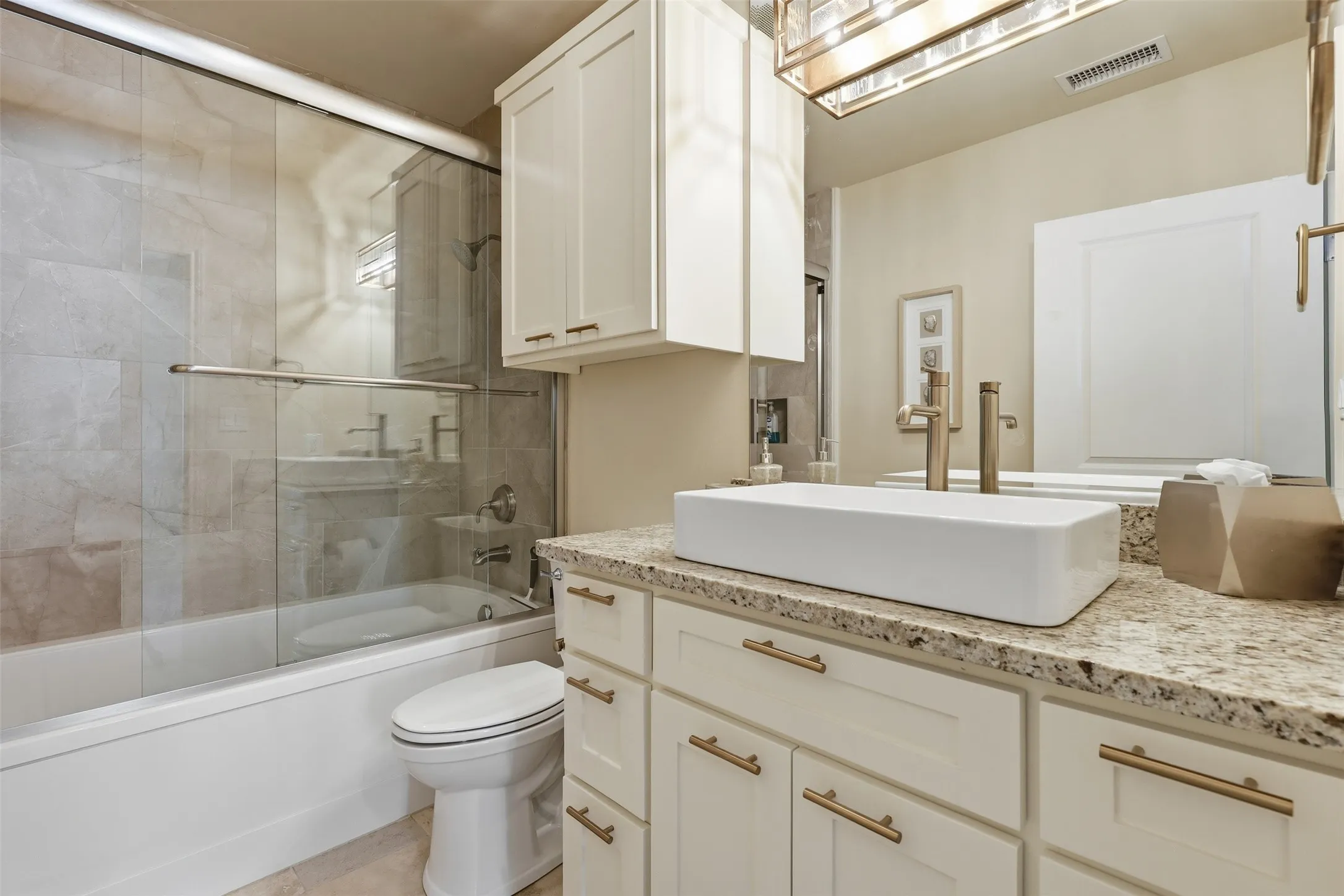 Shower-tub combination with glass enclosure, white vanity with stone countertop, rectangular vessel sink, and modern gold-toned faucet