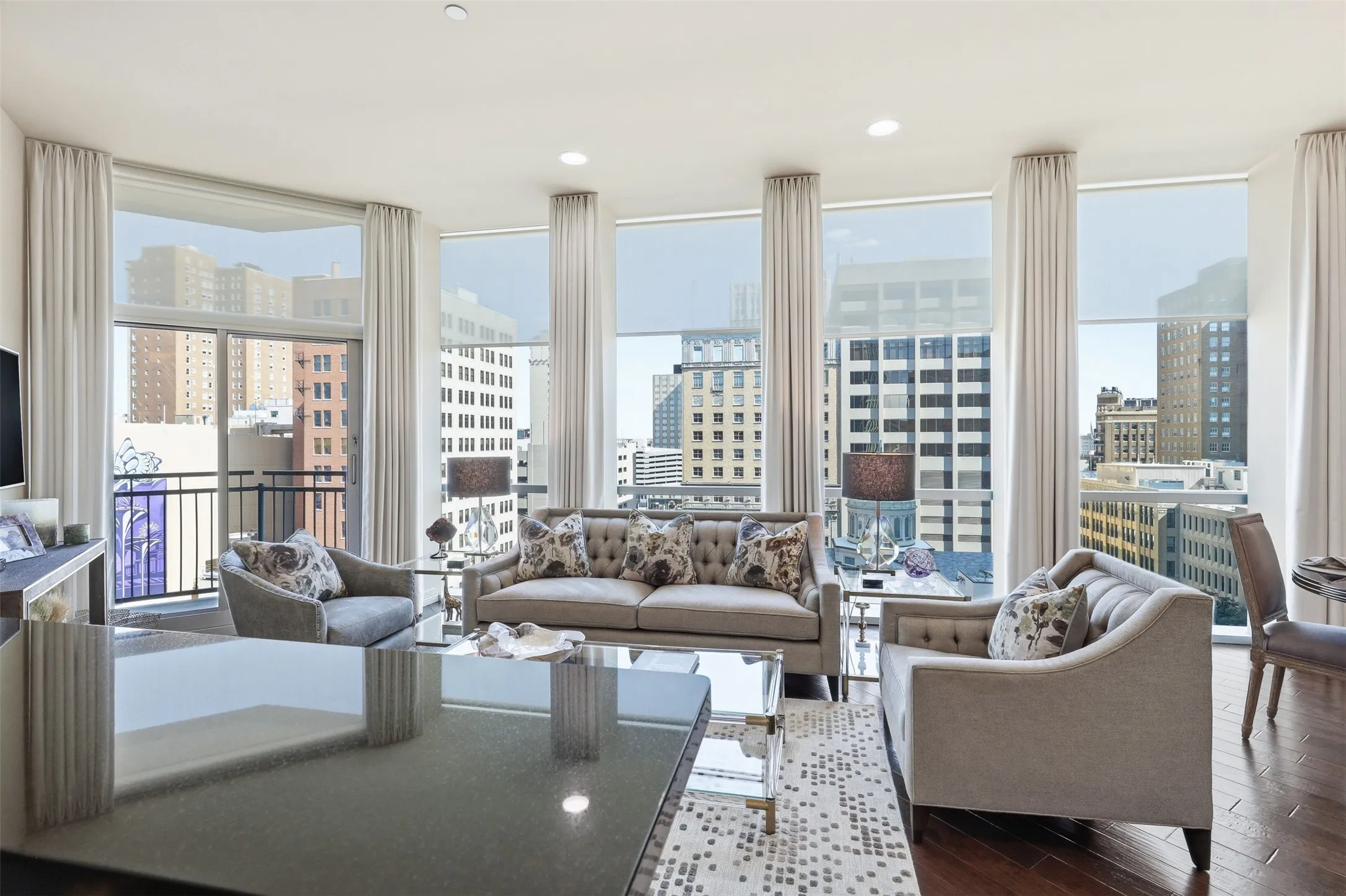 Hardwood flooring, floor-to-ceiling windows with roller shades, and a private balcony with city buildings