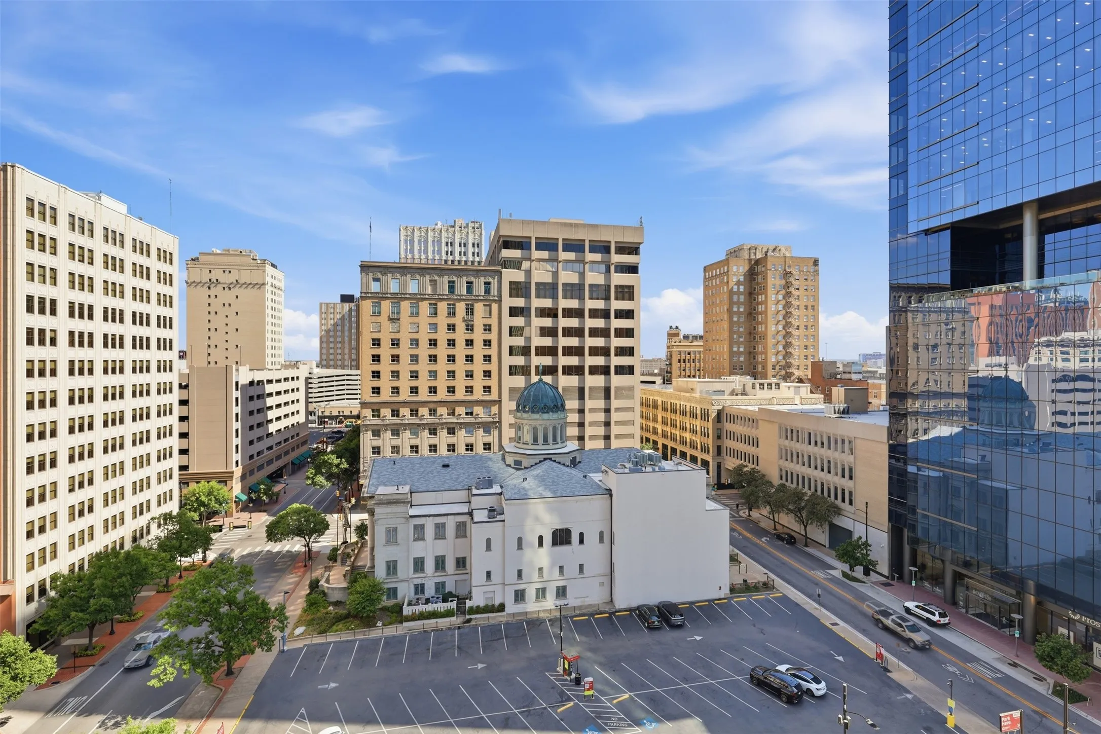 Cityscape featuring multiple high-rise buildings, a street with parked vehicles, and a prominent building with a domed roof