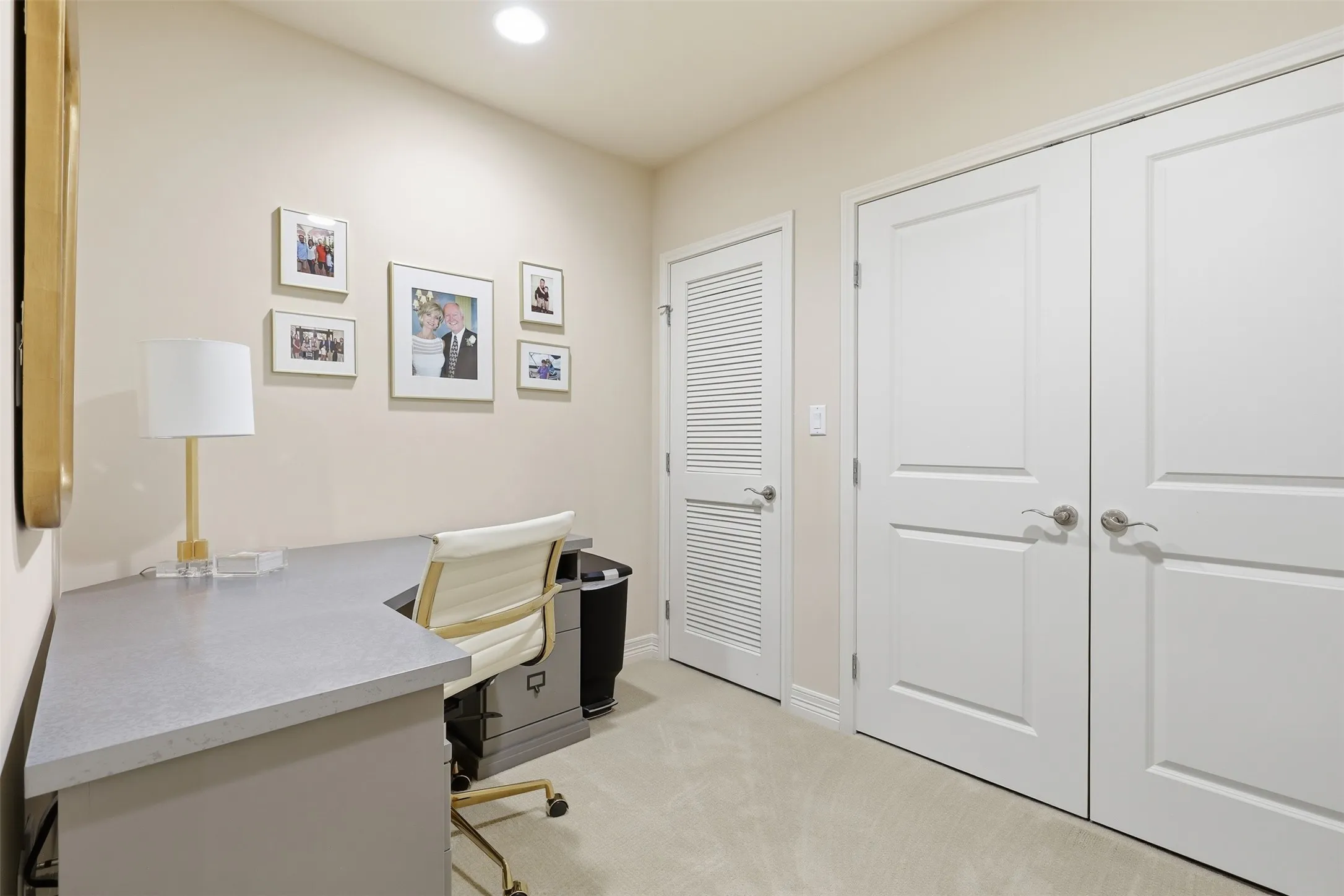 Recessed ceiling lighting, light-toned wall paint, neutral-toned carpeting, built-in desk with a gray surface, and paneled closet doors
