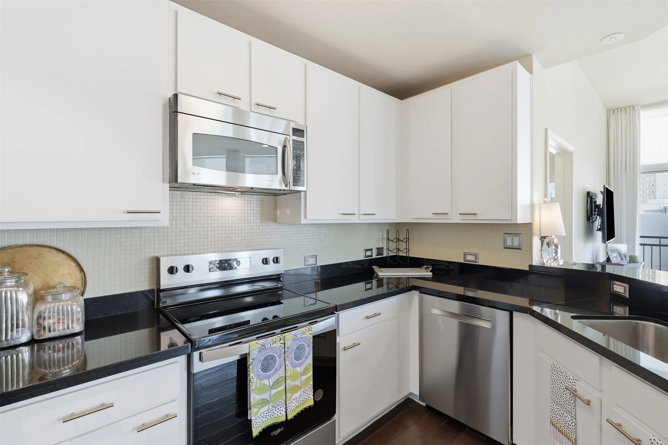 White cabinetry with brushed nickel hardware, stainless steel appliances, dark countertops, and tile backsplash