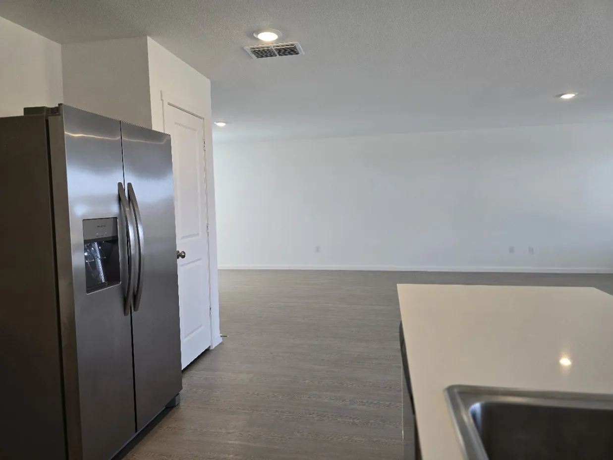 Stainless steel French door refrigerator, white solid surface countertop, stainless steel undermount sink, recessed lighting, and wood-finish flooring