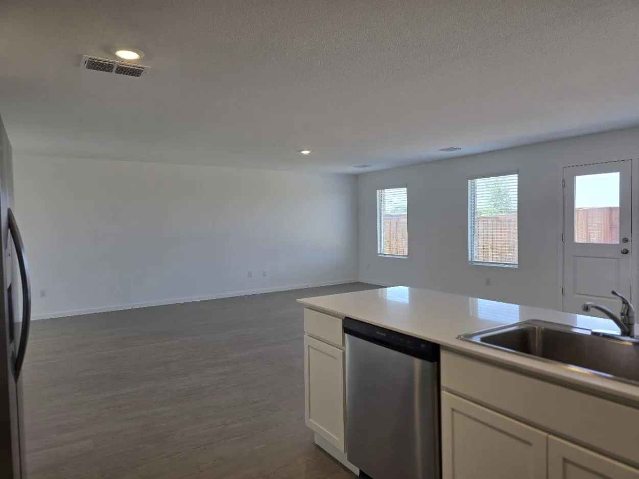 Kitchen island with a stainless steel sink and dishwasher, white cabinetry, and a light-colored countertop