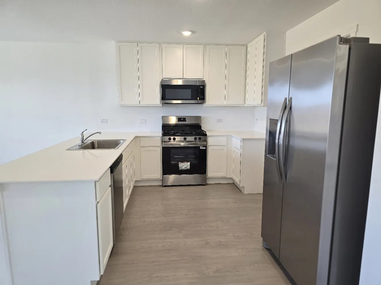U-shaped kitchen with white cabinetry, brand new stainless steel appliances, quartz countertops, and LVP flooring