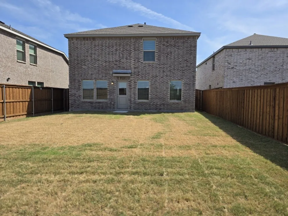 Brick exterior with multiple windows and a rear entry door, surrounded by a wood privacy fence