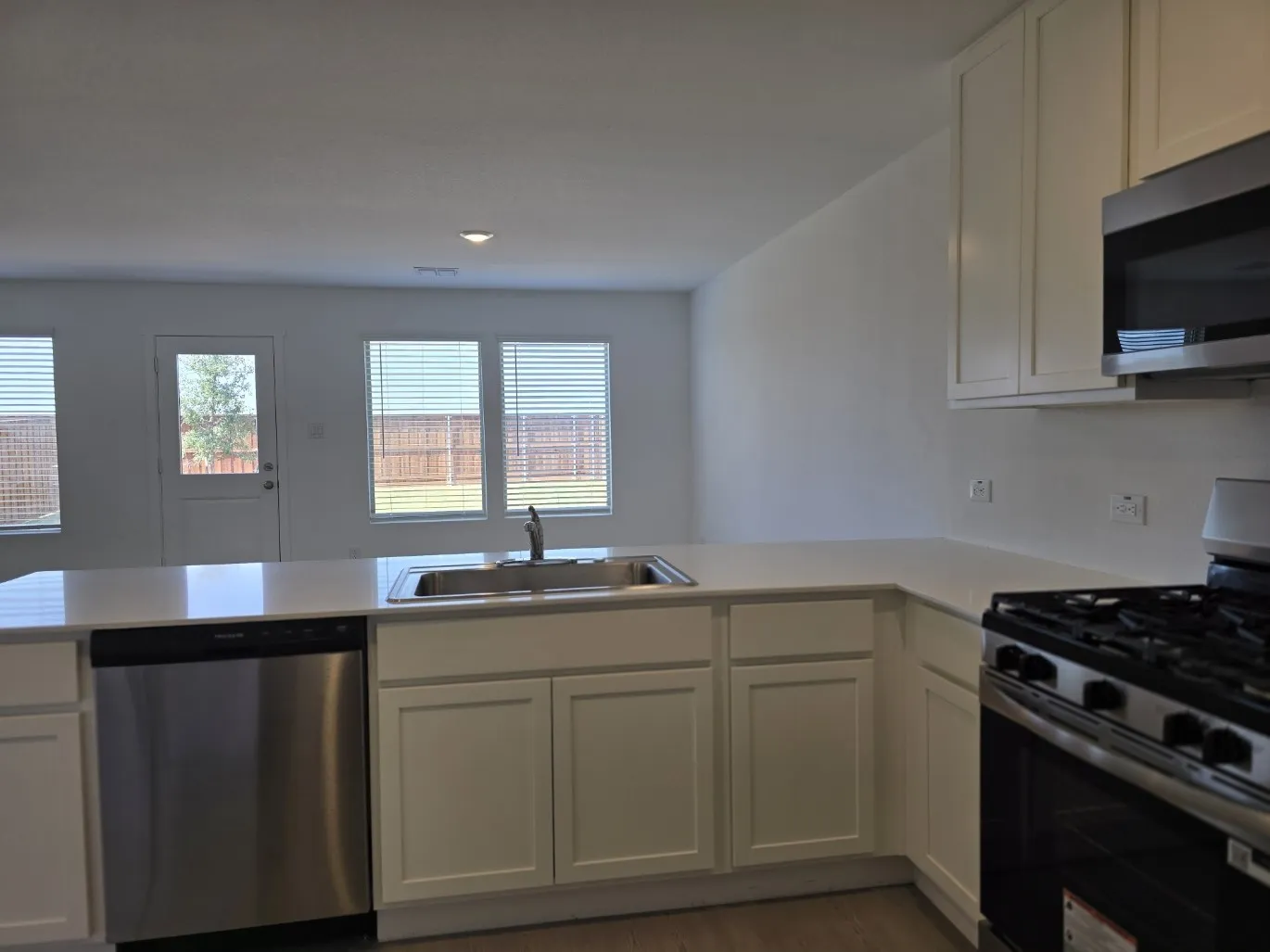Kitchen featuring white cabinetry, quartz countertops, stainless steel sink, stainless steel dishwasher, and 5 burner stainless steel gas range, microwave