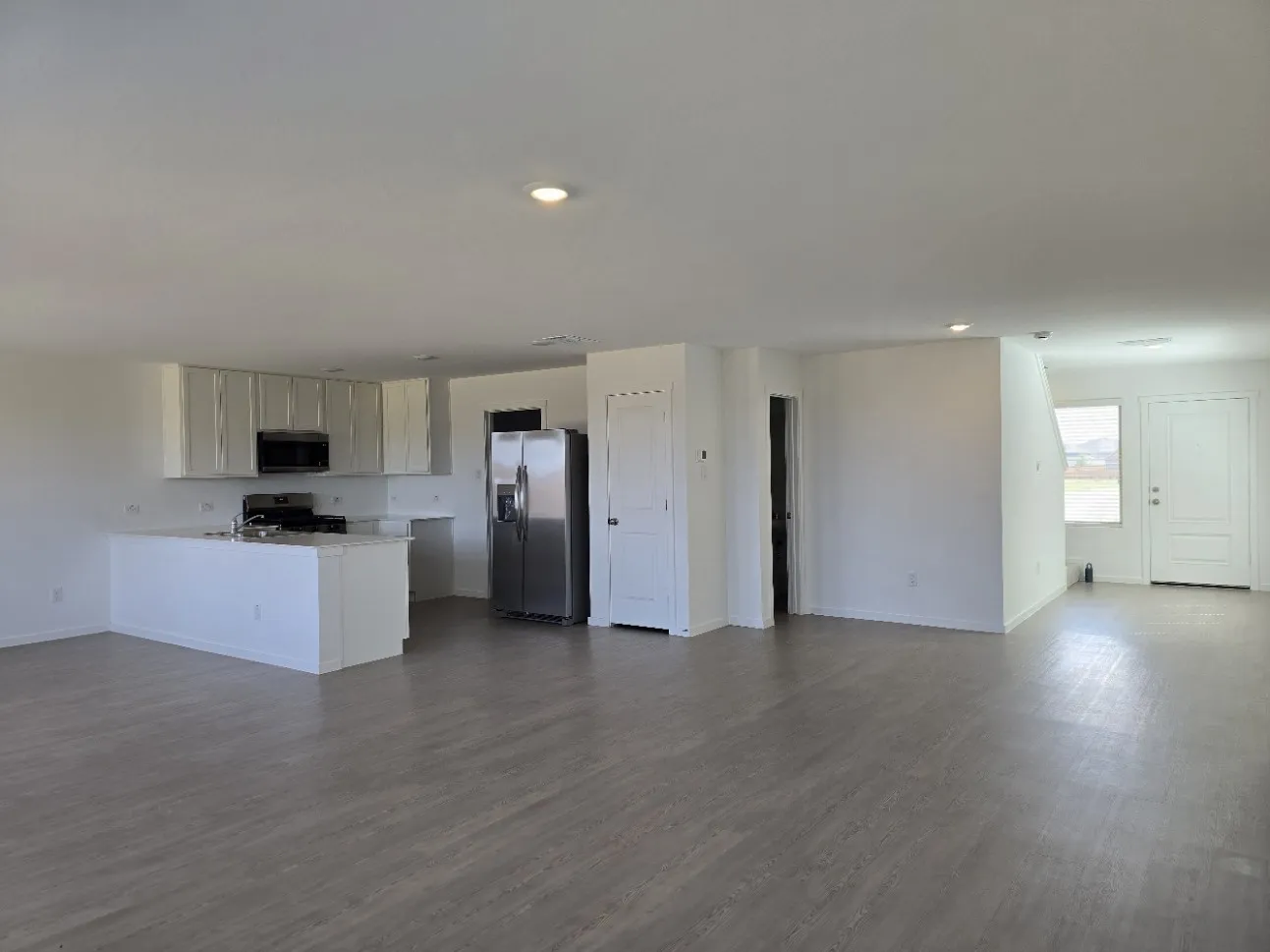 Open concept living area featuring LVP flooring throughout, recessed lighting, and a kitchen island with quartz countertop, shows a peak of the 1/2 bathroom, and front door entry.