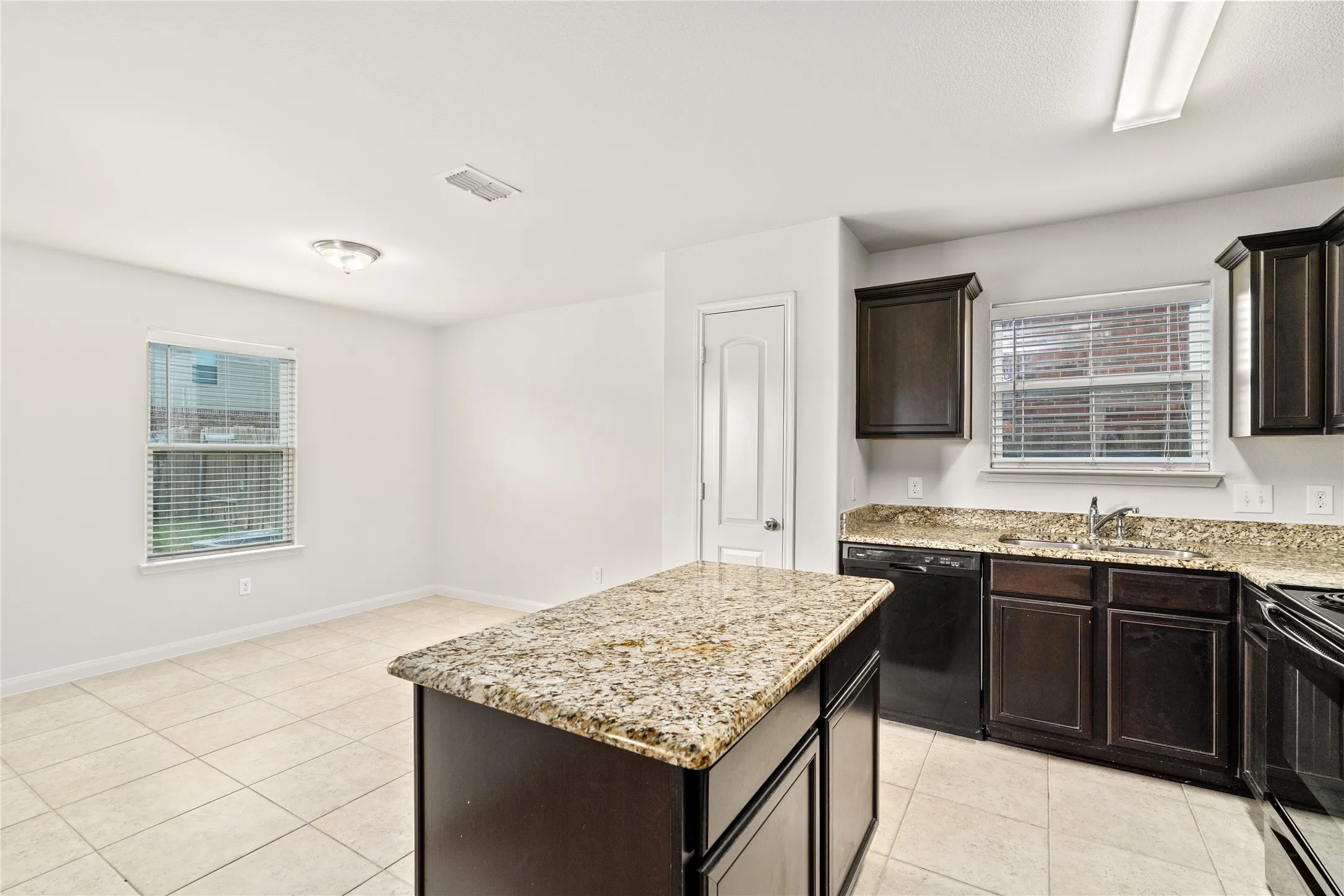 Kitchen featuring an island with stone countertop, dark wood cabinetry, black appliances, and tile flooring