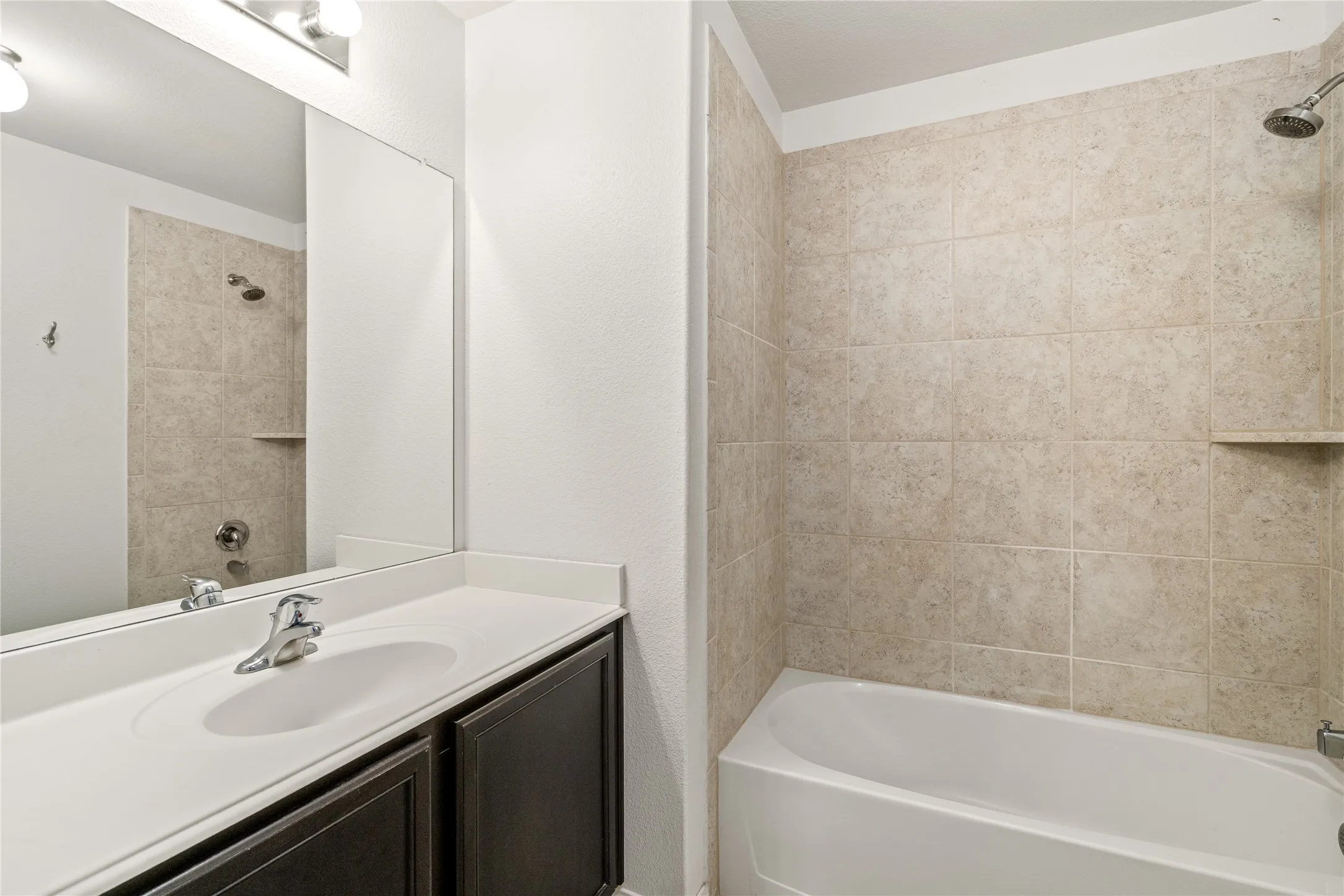 White tub with tiled surround, built-in shower niche, and wall-mounted showerhead