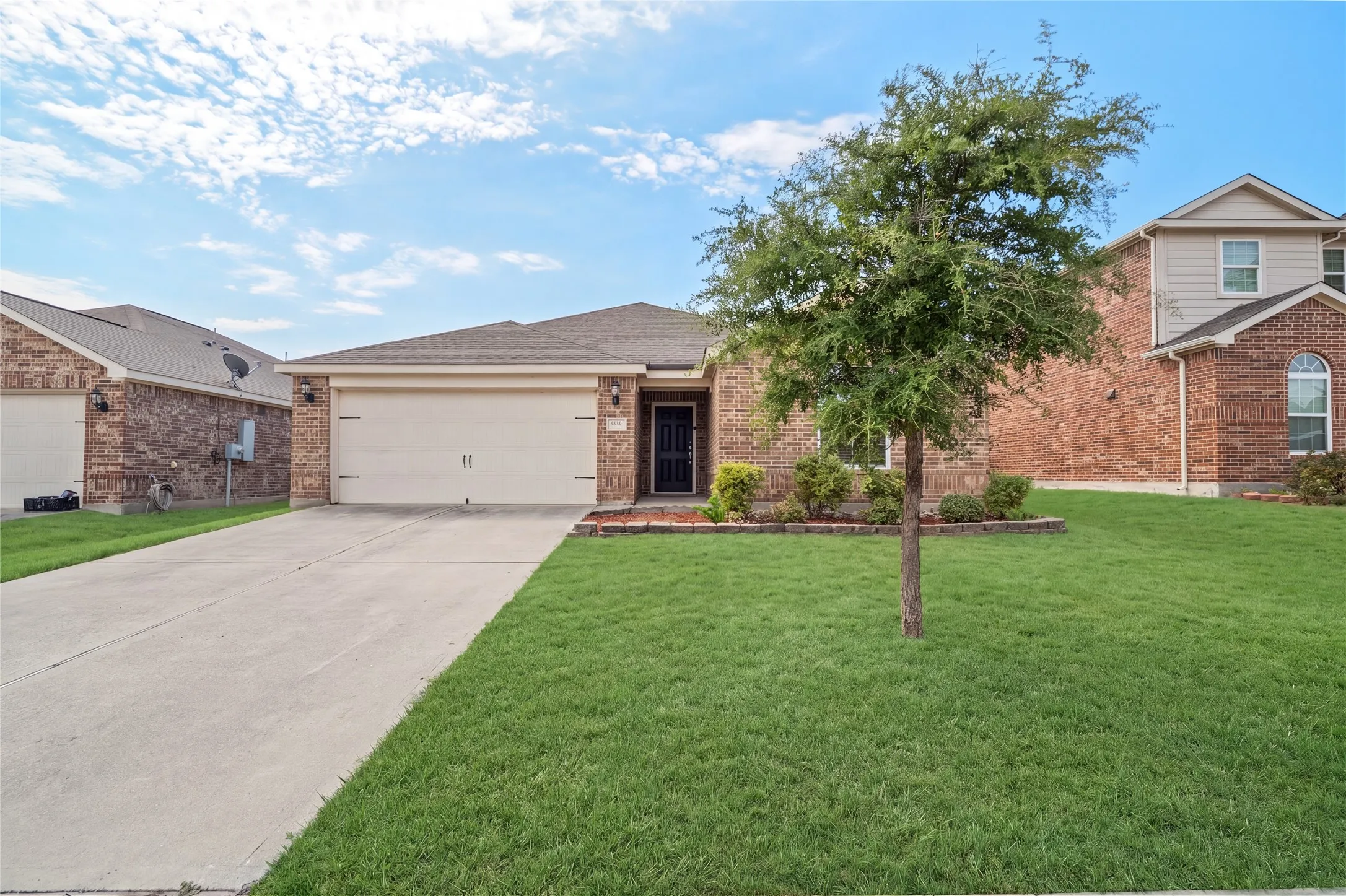 Brick exterior with a two-car garage, concrete driveway, and a front yard featuring a tree and shrubbery