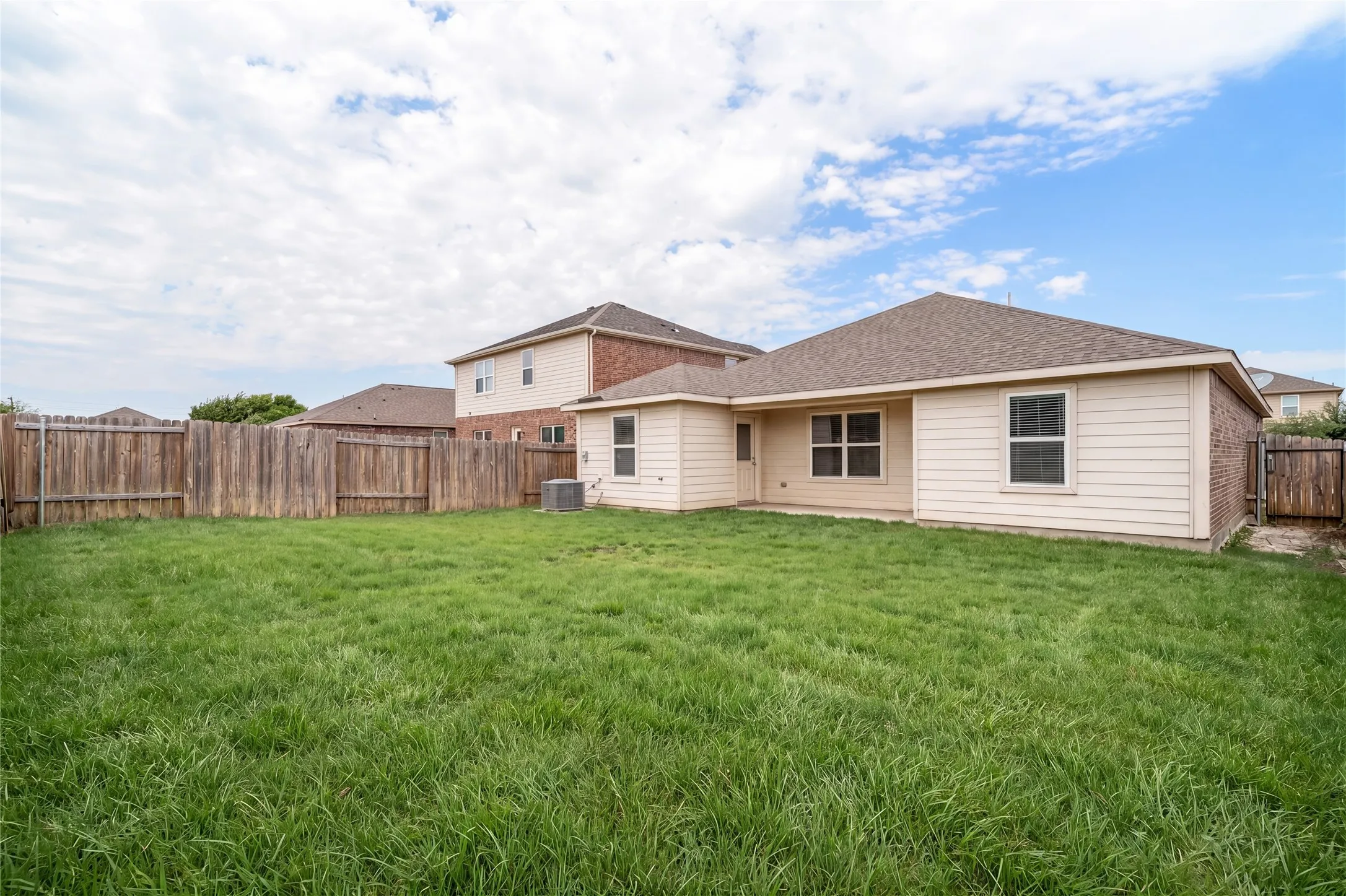 Expansive grass yard with wood fencing and a single-story residence featuring siding and brick accents