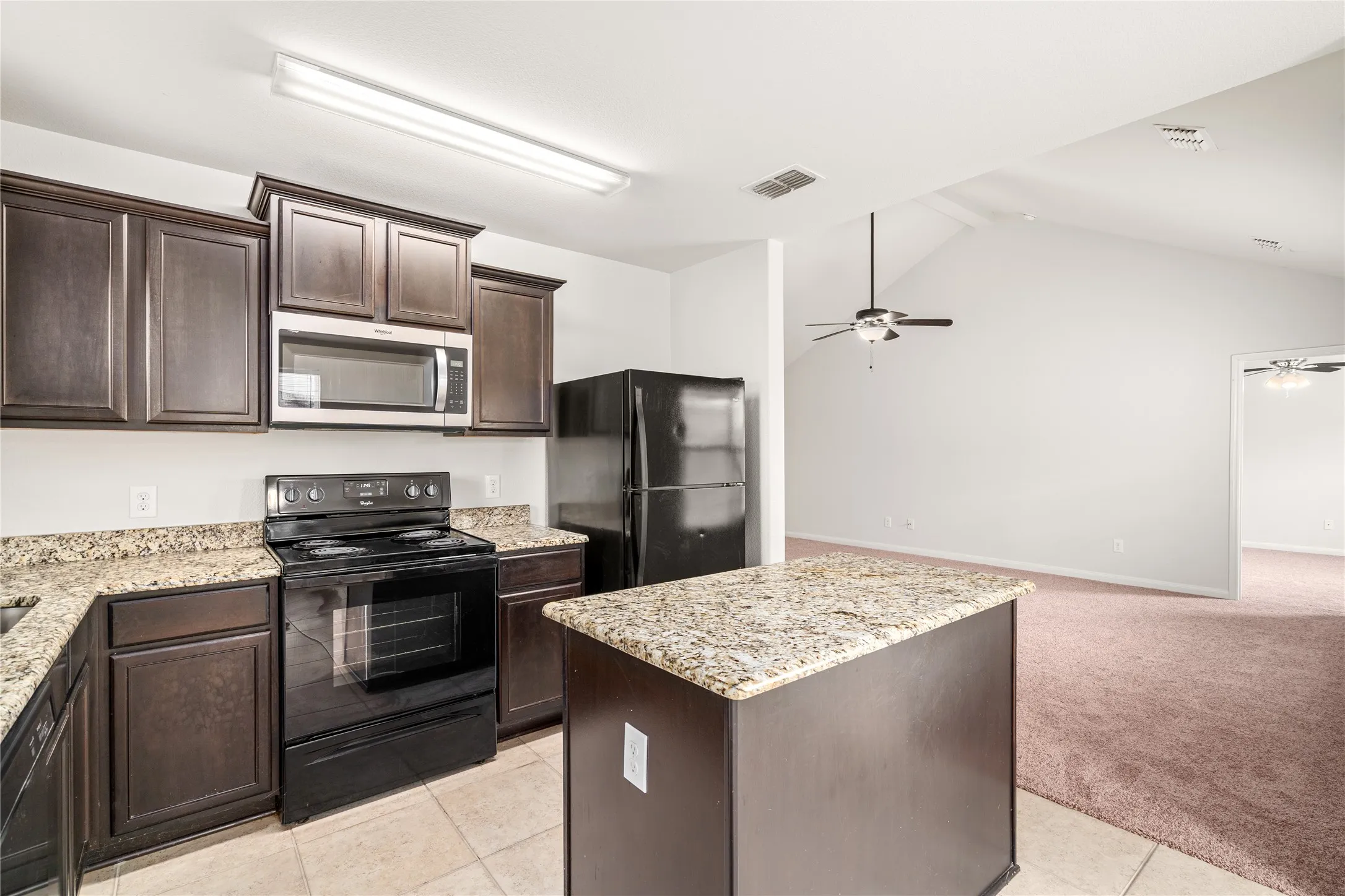 Kitchen featuring dark wood cabinetry, stainless steel microwave, black range, black refrigerator, and granite-style countertops