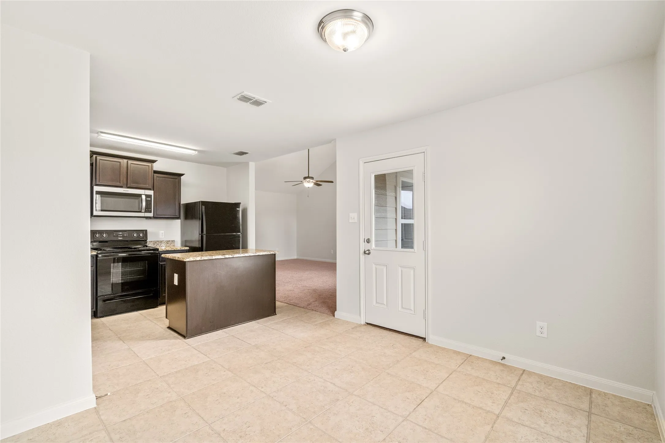 Kitchen featuring dark wood cabinetry, black appliances, a central island with a stone-finish countertop, and tile flooring