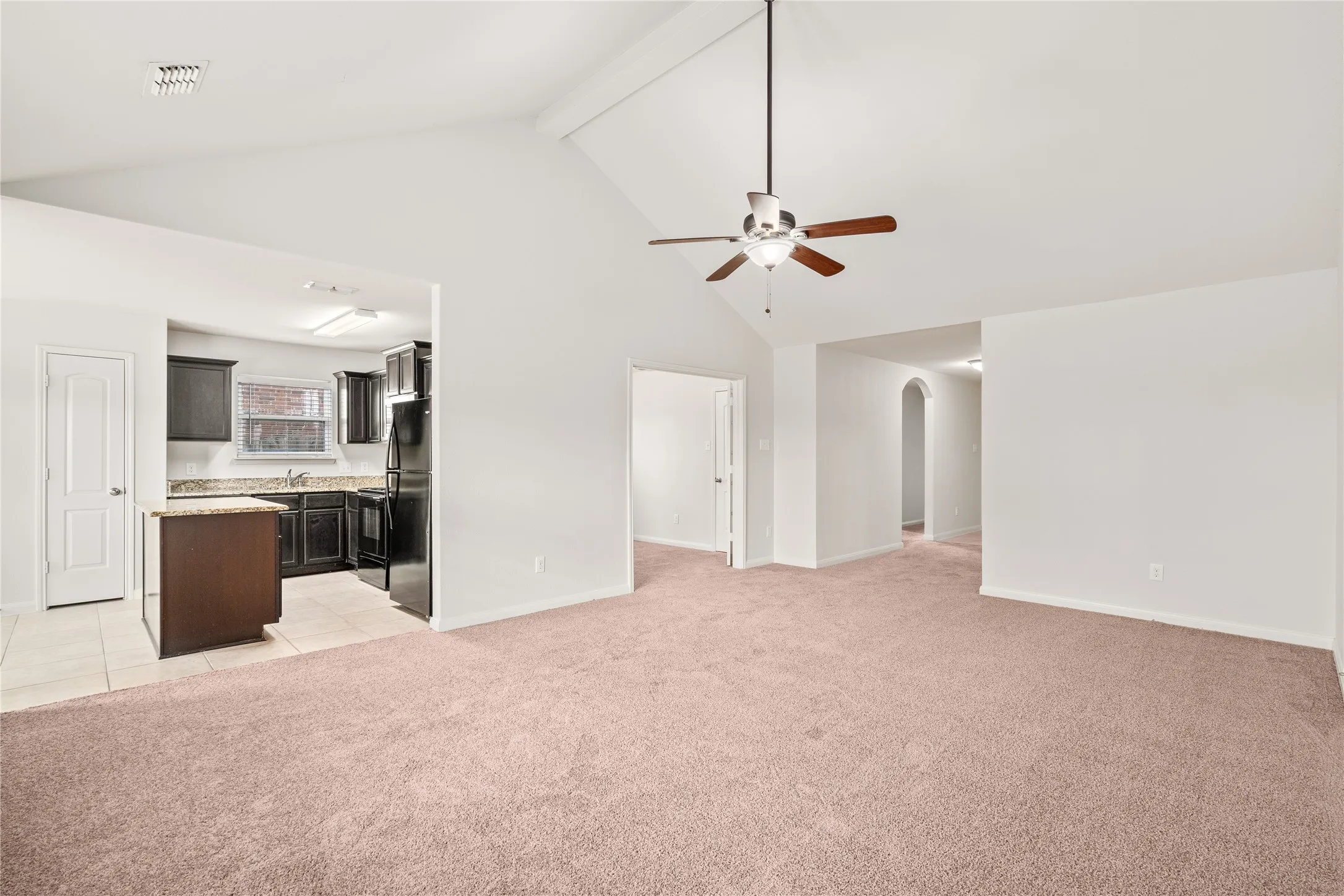 Vaulted ceiling with a ceiling fan, recessed lighting, dark wood-finish cabinetry, black appliances, and a kitchen island with a stone-finish countertop