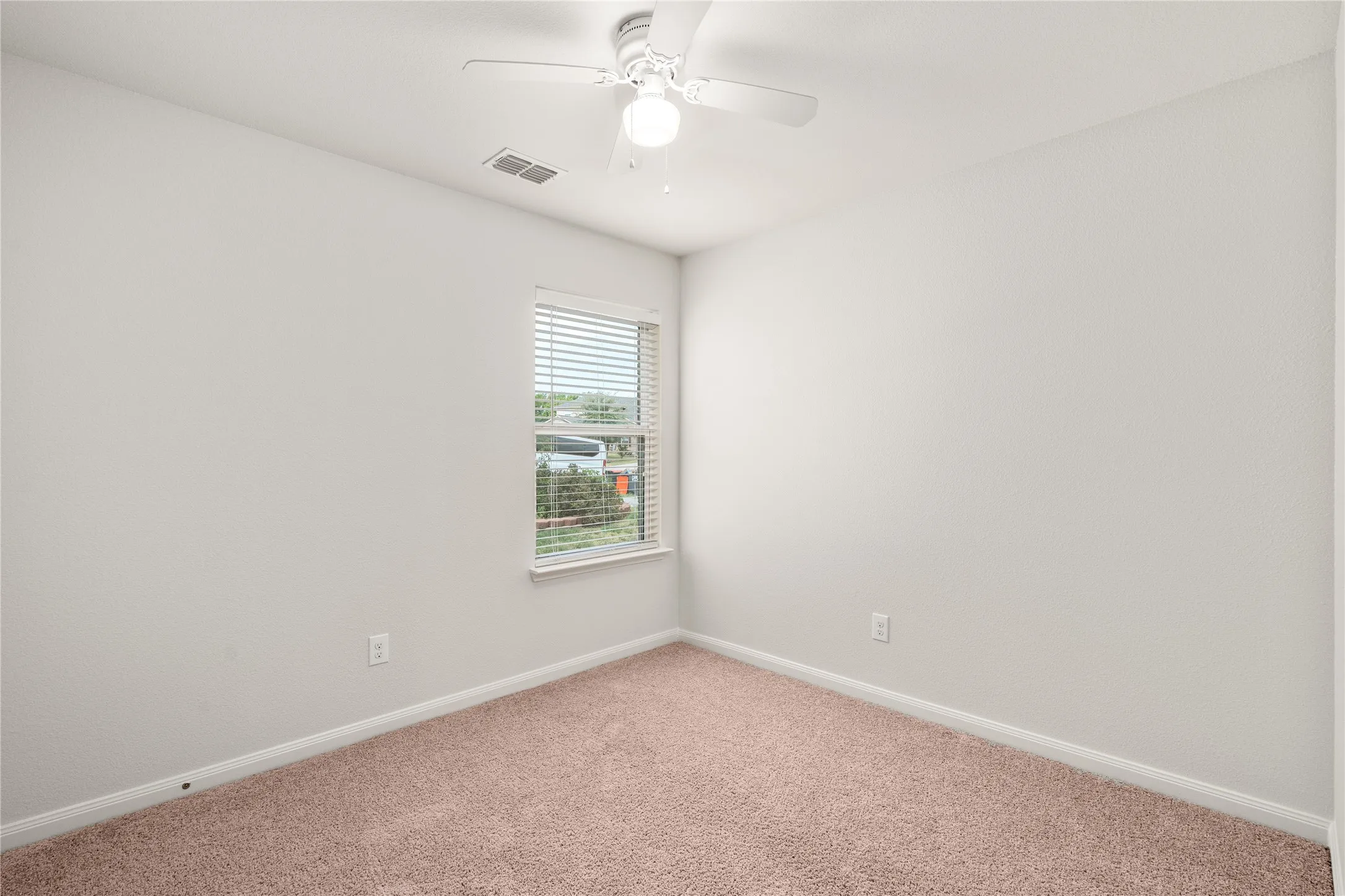 Bright bedroom with neutral wall finishes, carpeted flooring, ceiling fan with integrated lighting, and a large window with blinds providing natural illumination
