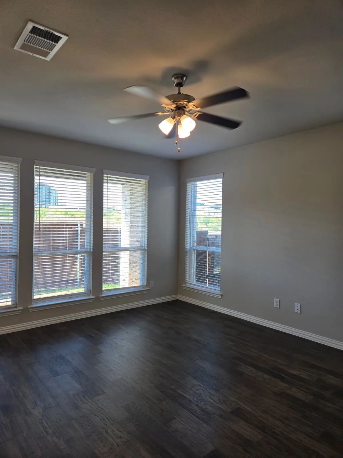 Wood-finish flooring, multiple windows with blinds, ceiling fan with integrated lighting, and light-toned wall paint