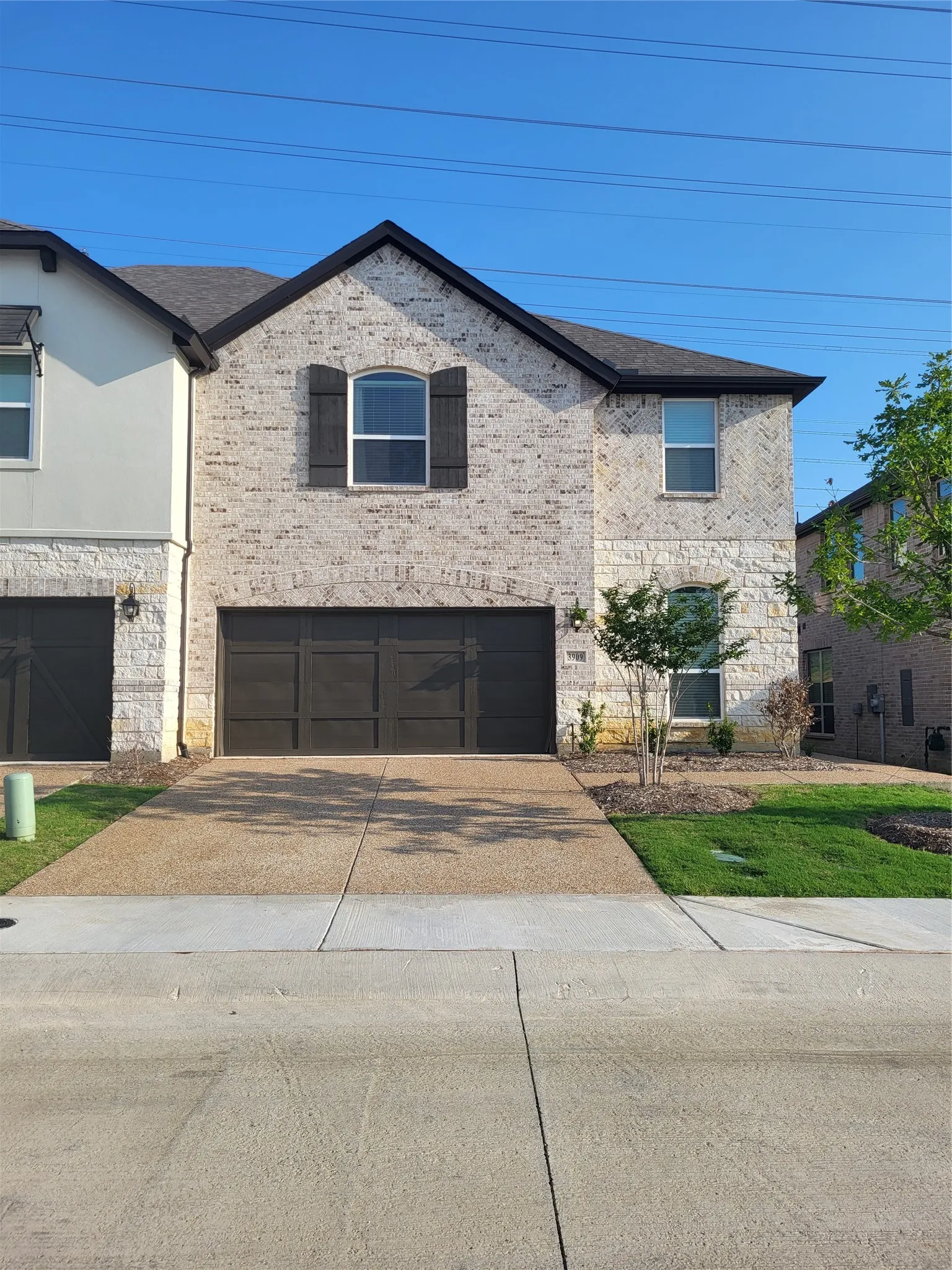 Stone and brick exterior with dark shutters, an arched window, a two-car garage, and a concrete driveway