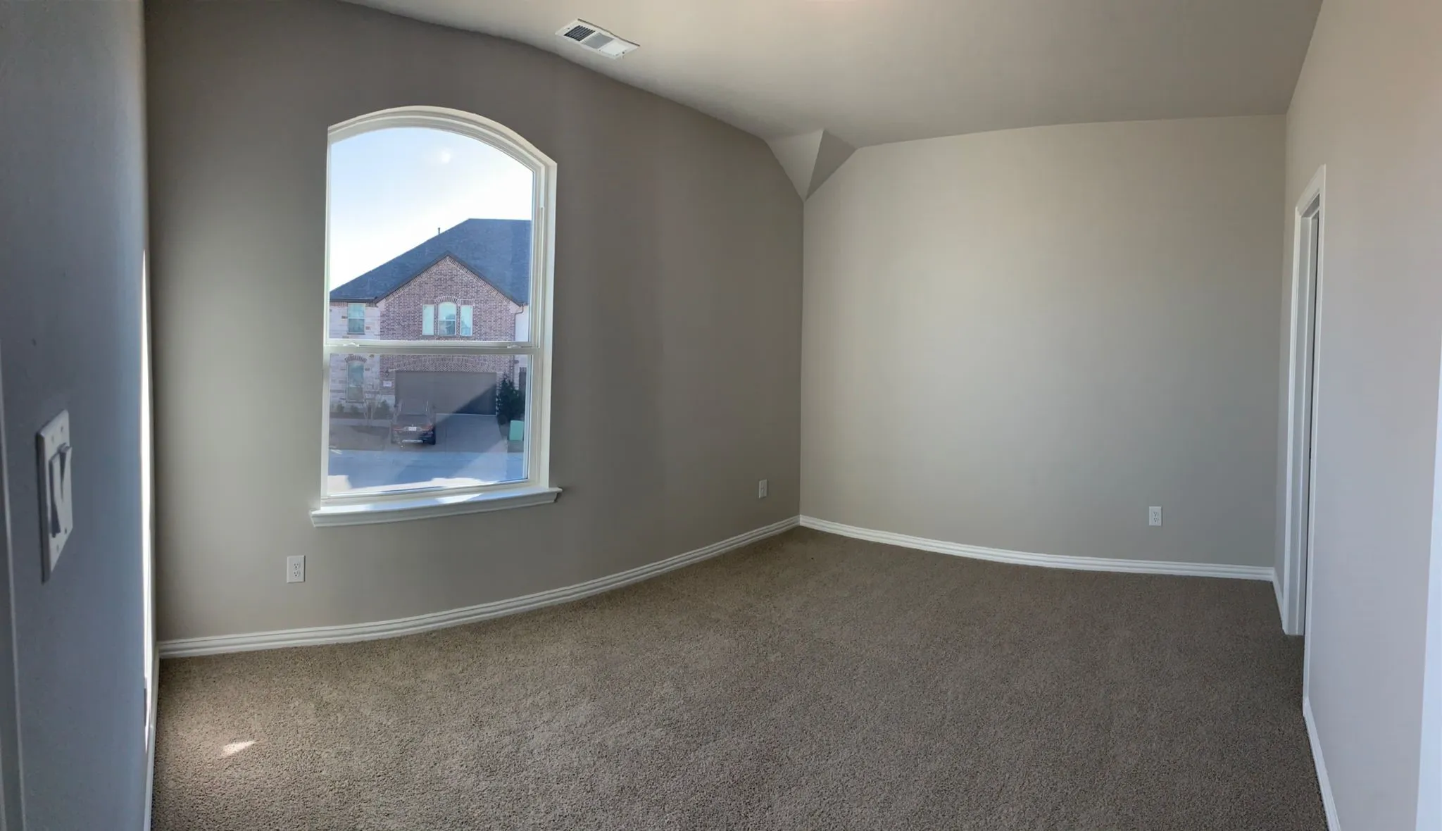 Arched window, neutral tone carpeting, painted walls, vaulted ceiling, and white trim