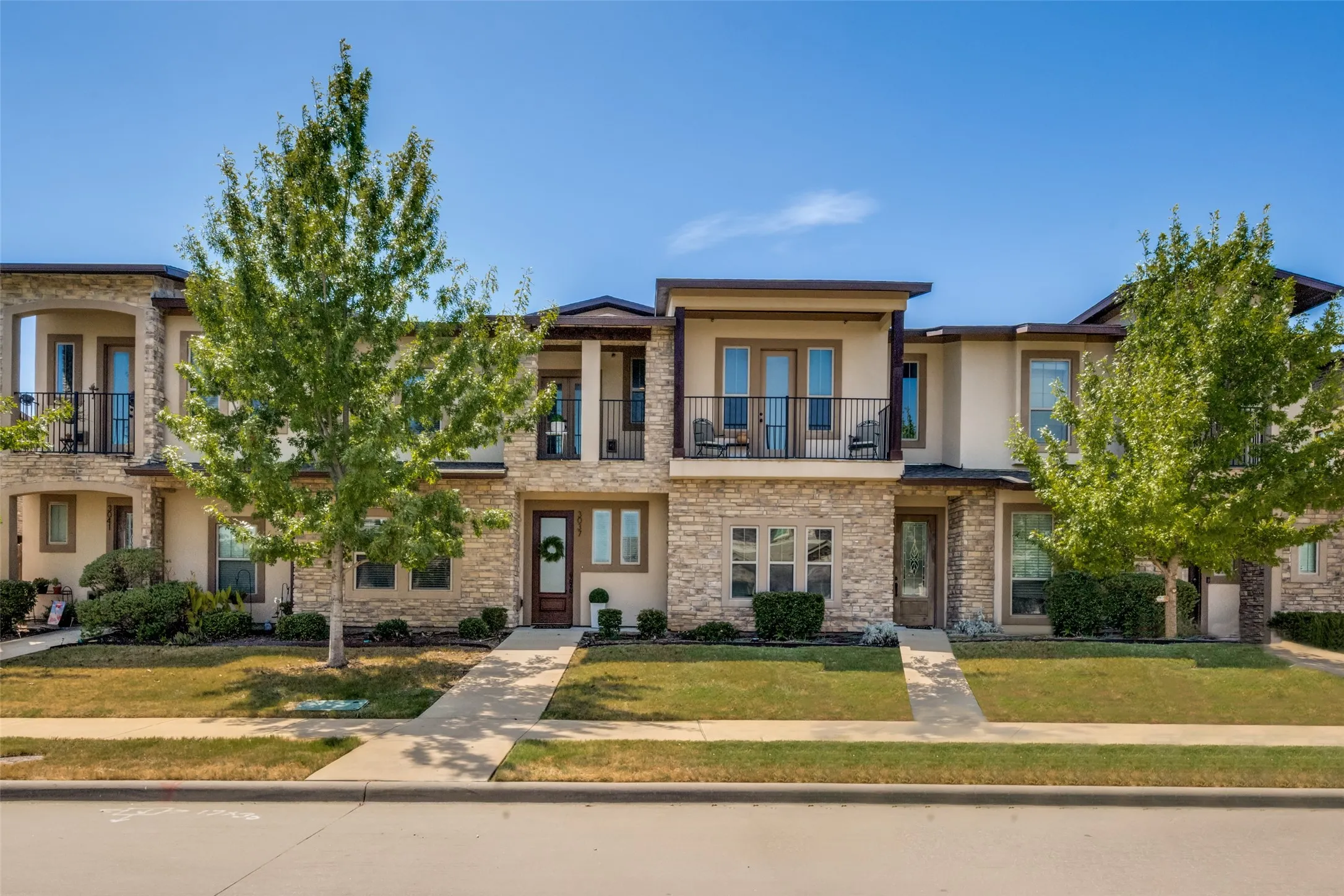 Contemporary stucco and stone exterior featuring multiple balconies, a covered entryway, and mature landscaping