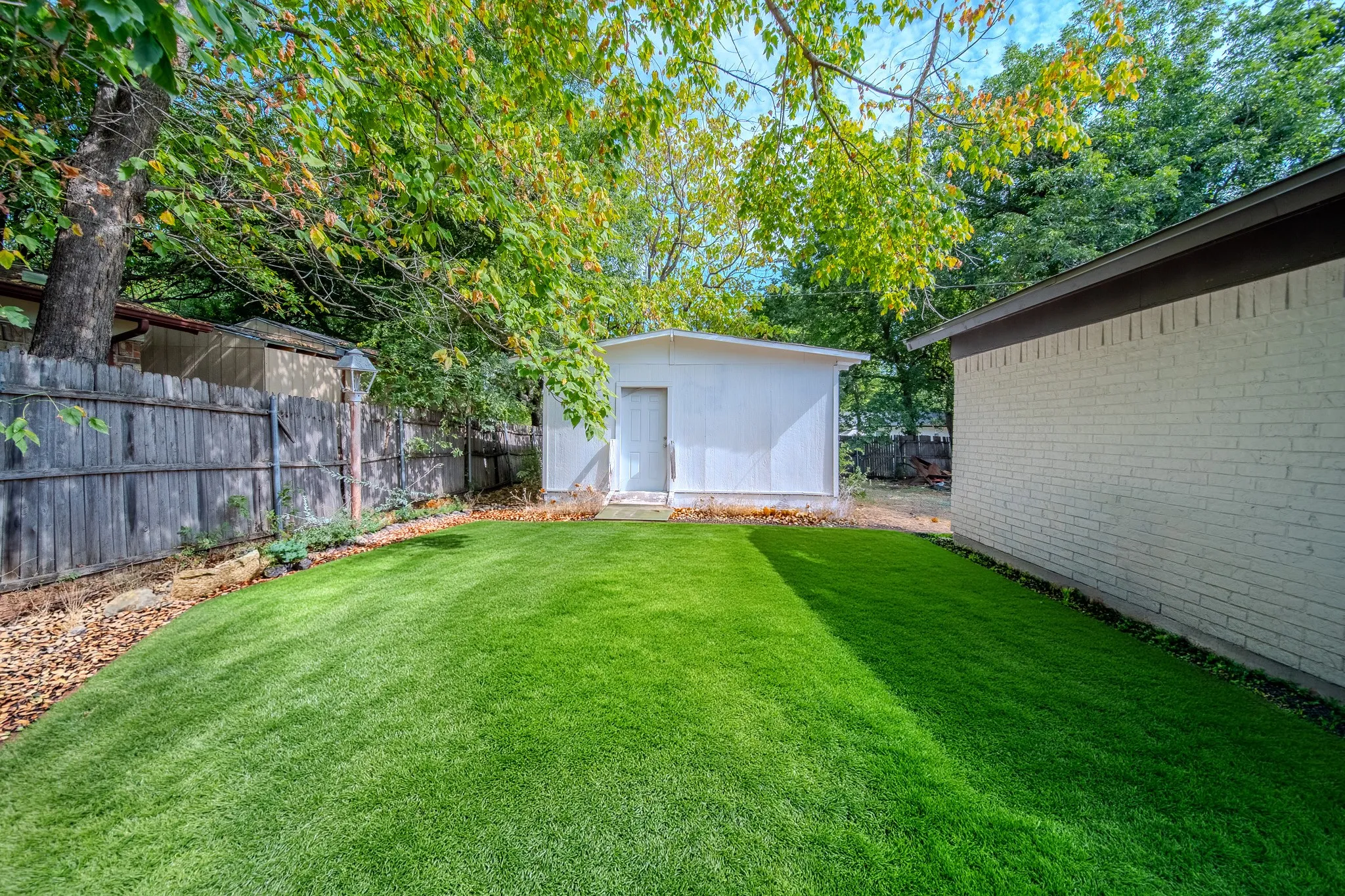 Expansive lawn area with a white detached storage structure