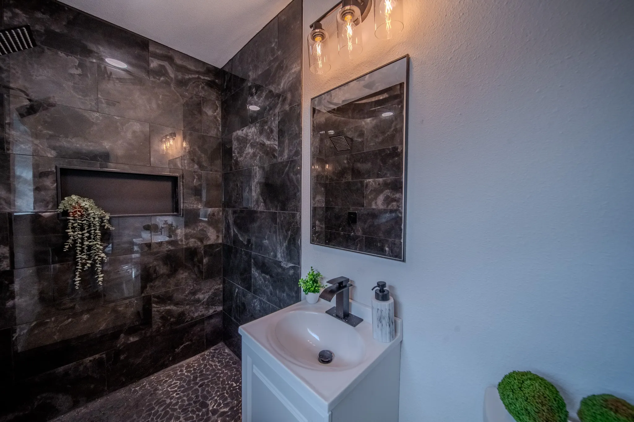 Shower with dark marble-look wall tiling, rain showerhead, and recessed niche