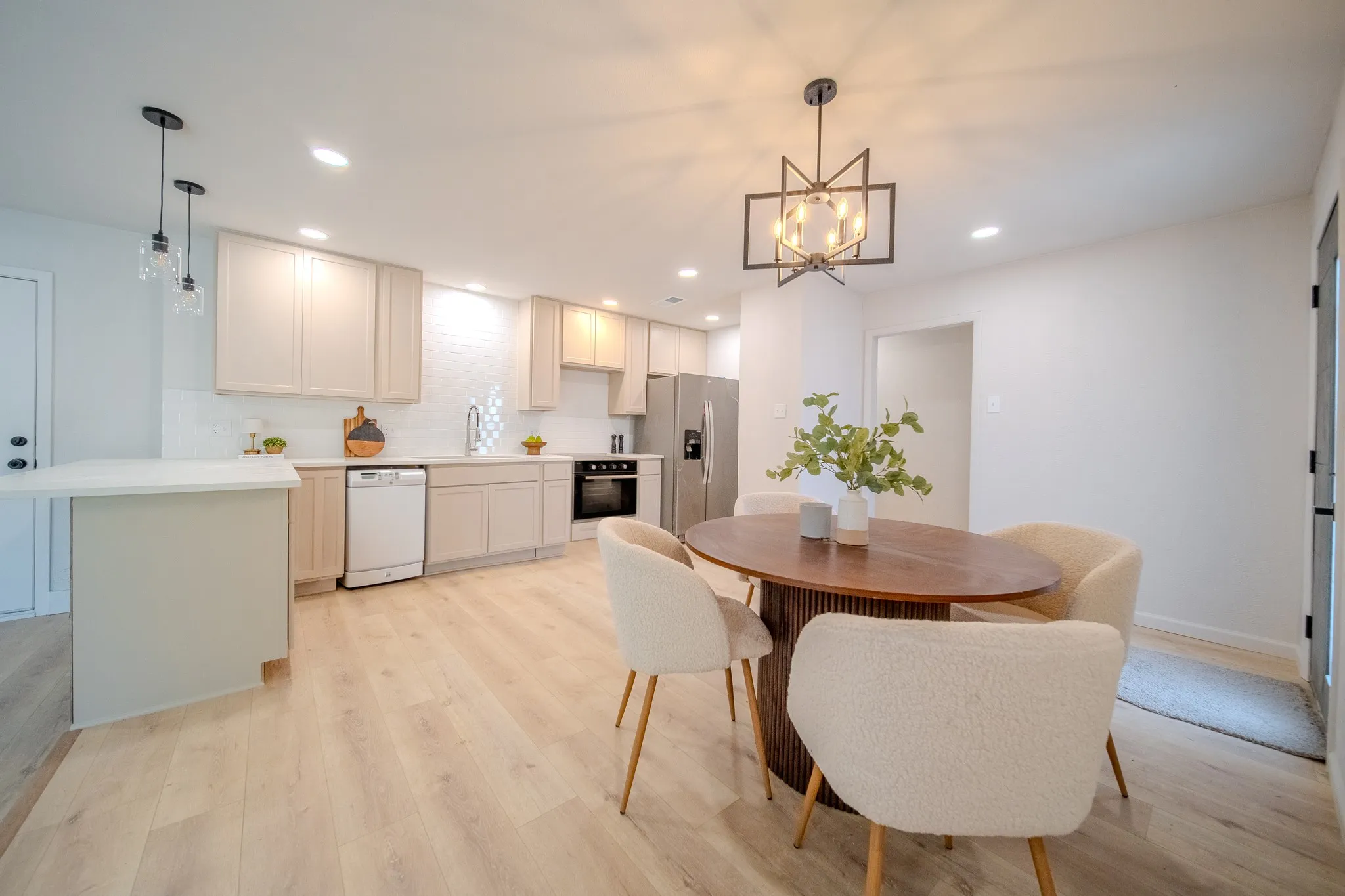Kitchen featuring light-toned cabinetry, white subway tile backsplash, stainless steel appliances, and a light wood-finish flooring