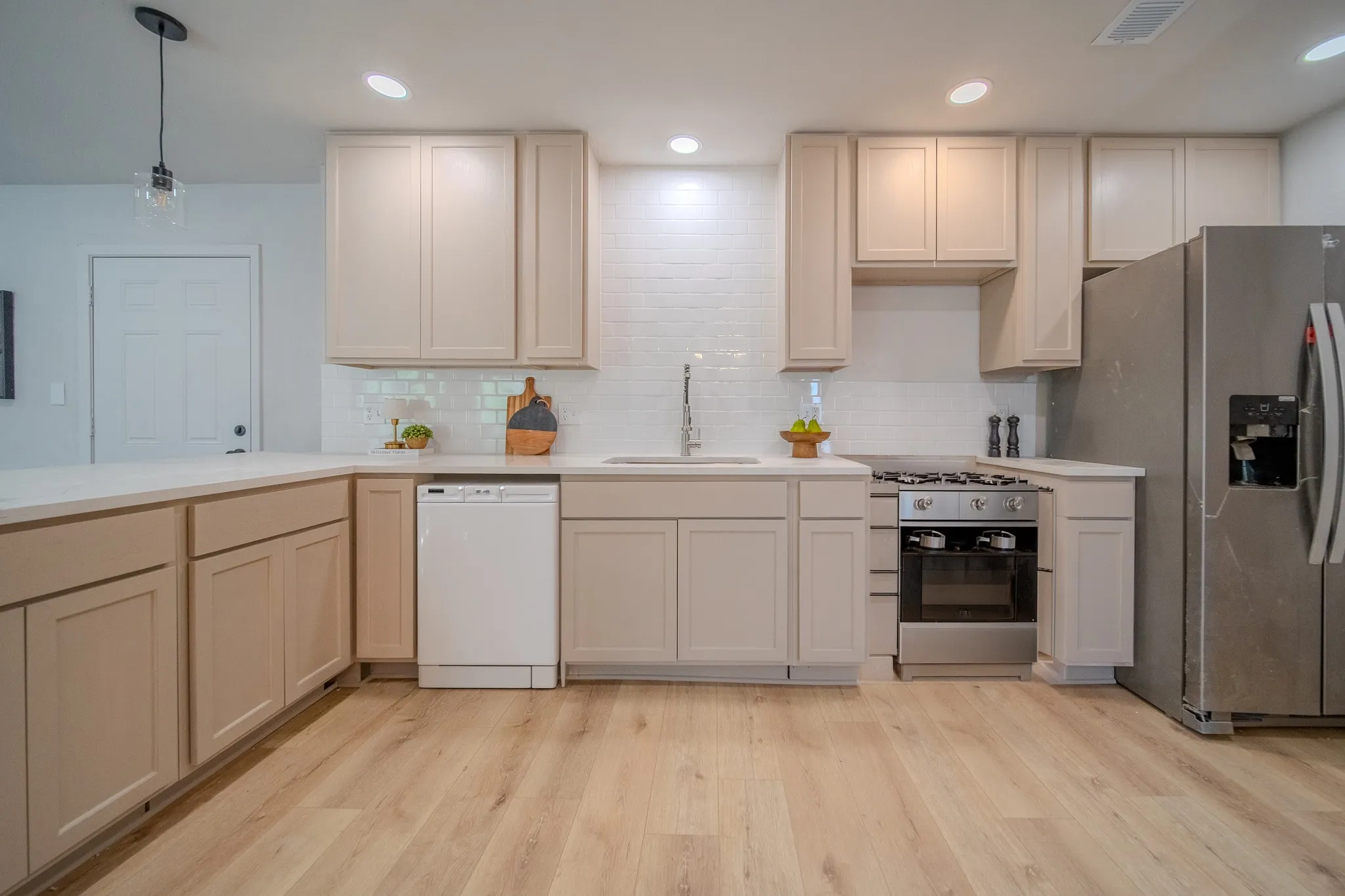 Kitchen featuring light wood-finish flooring, white countertops, subway tile backsplash, and stainless steel appliances