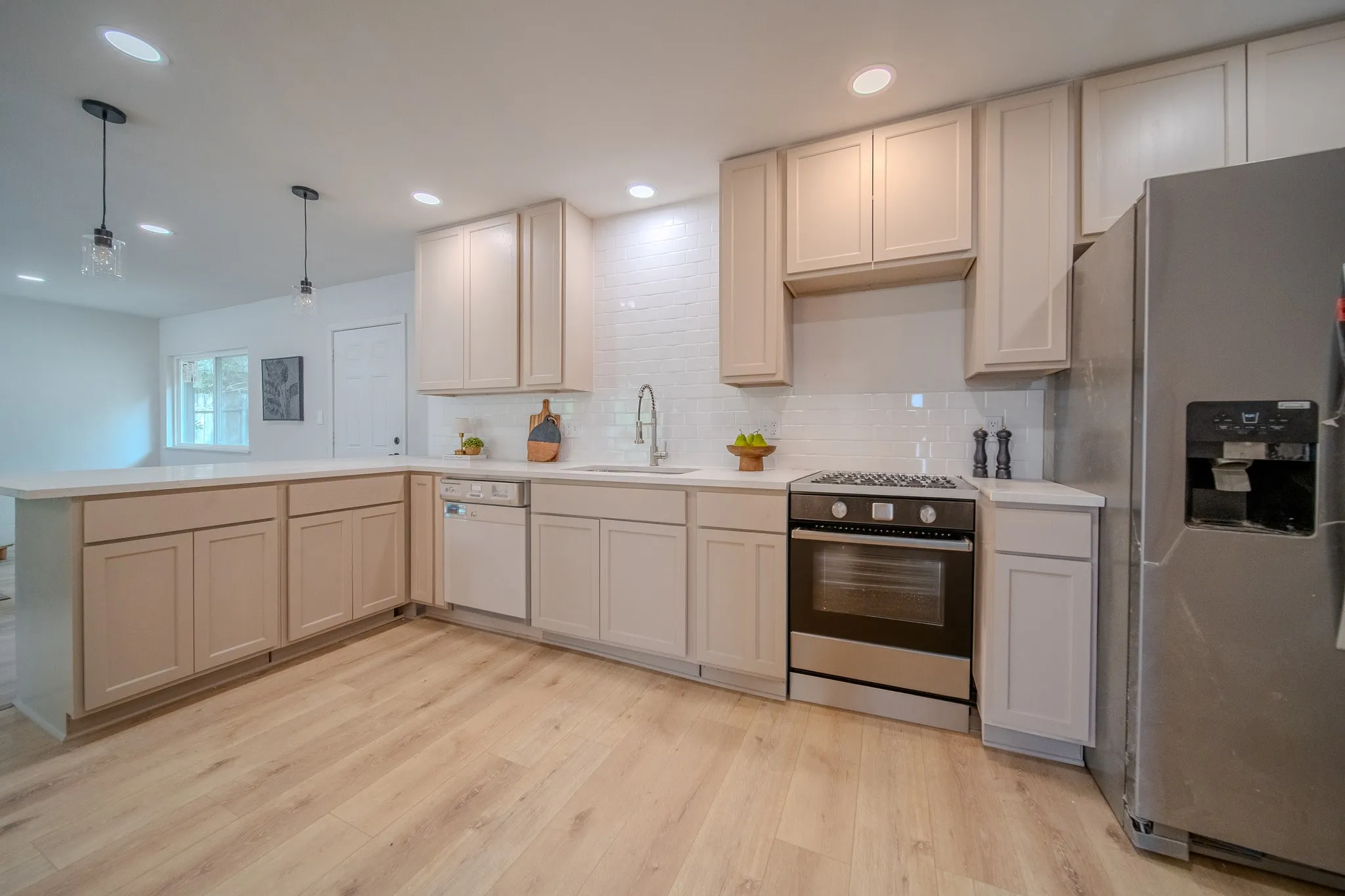 Contemporary kitchen featuring light wood-finish flooring, white countertops, a subway tile backsplash, and stainless steel appliances