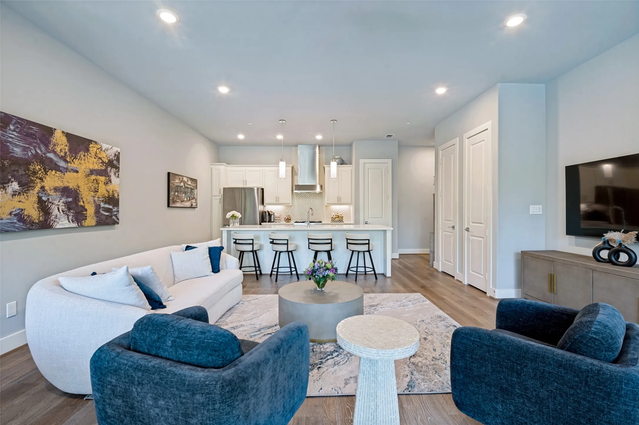 Open-concept living space featuring wood-finish flooring, recessed lighting, white kitchen cabinetry, stainless steel appliances, and a kitchen island with seating