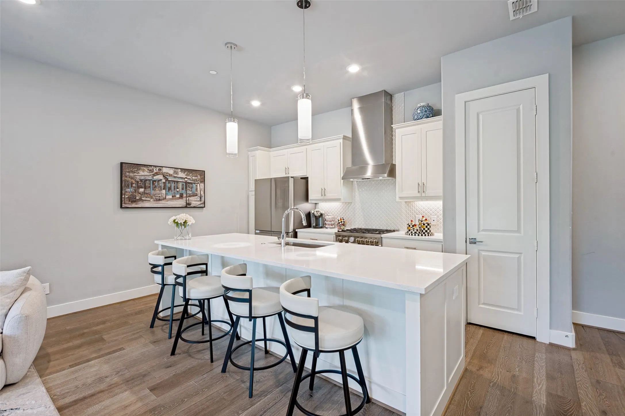 Open-concept kitchen featuring an island with a light-toned countertop, stainless steel appliances, white cabinetry, and wood-finish flooring