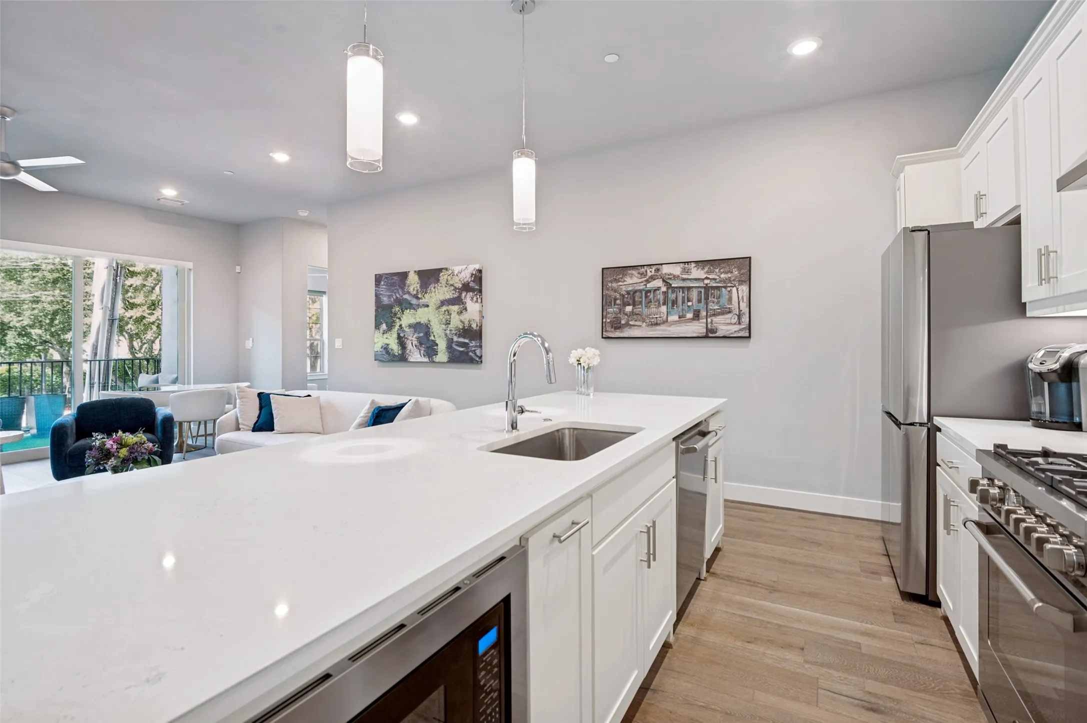 Gourmet kitchen featuring a large central island with an undermount sink, stainless steel appliances, white cabinetry, and wood-finish flooring