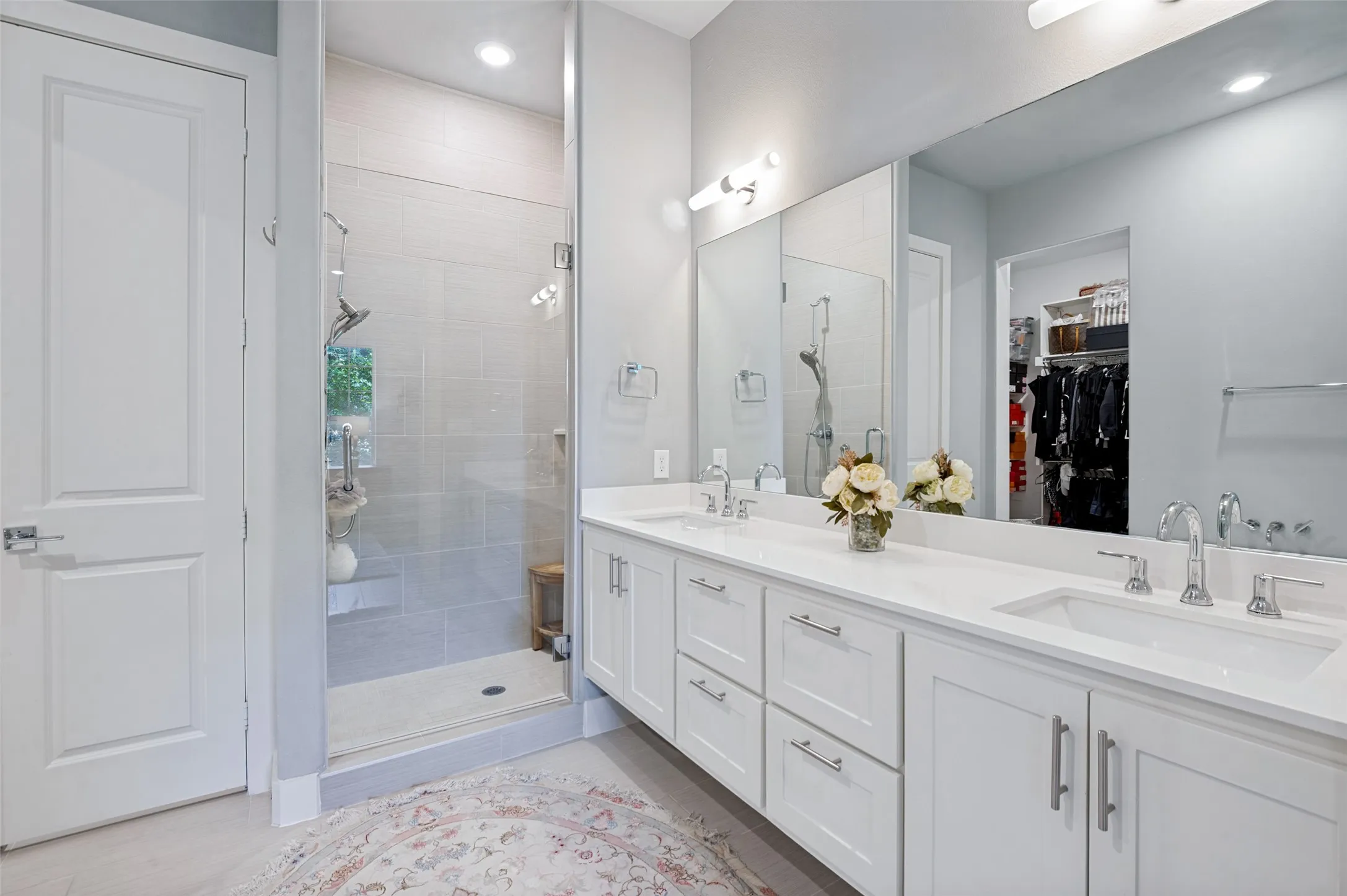 Dual vanity with white cabinetry, polished chrome fixtures, expansive mirror, and glass-enclosed shower