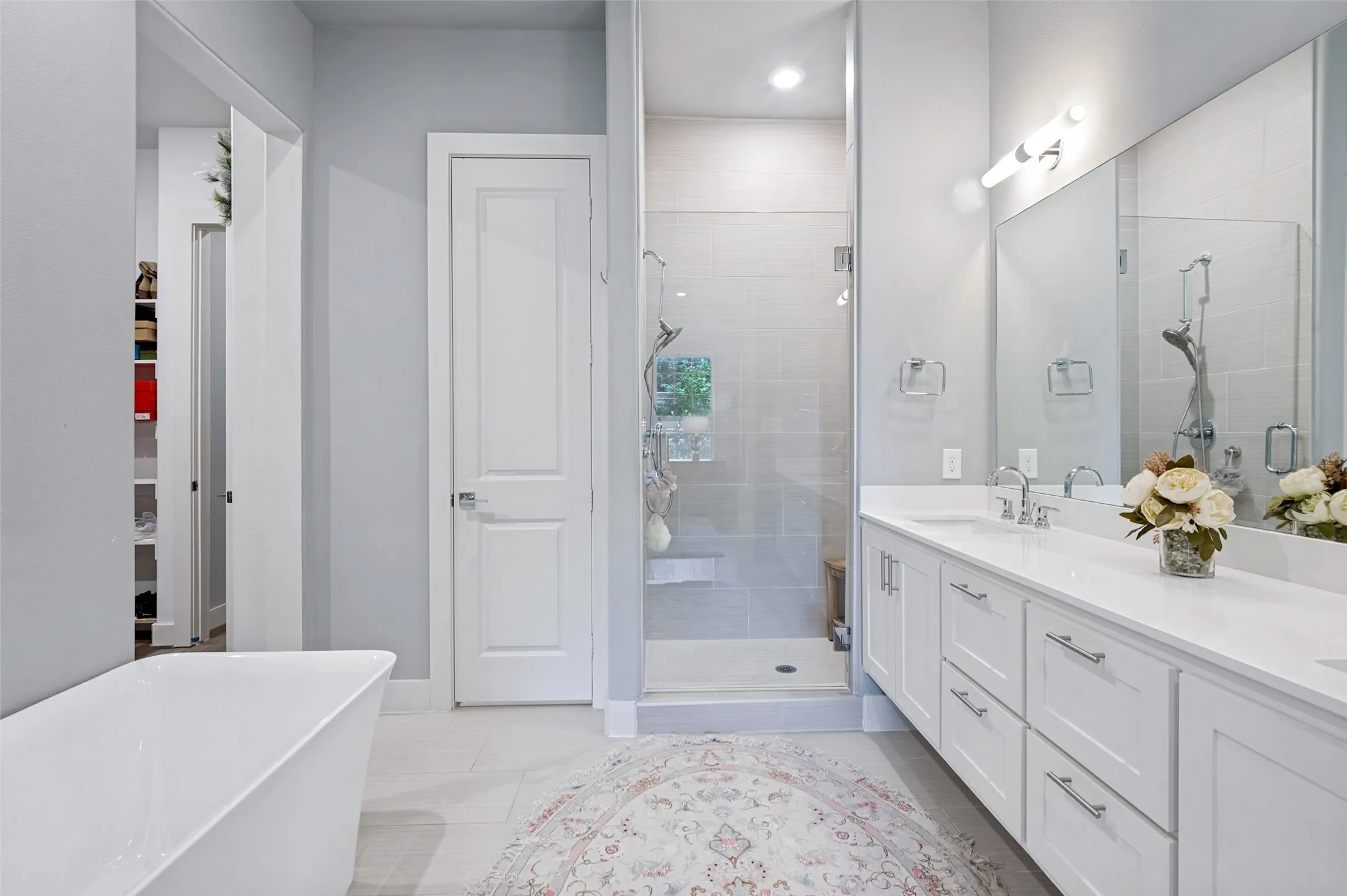 Freestanding soaking tub, glass-enclosed shower with tiled surround, double vanity with white cabinetry, polished chrome fixtures, and a large wall-mounted mirror