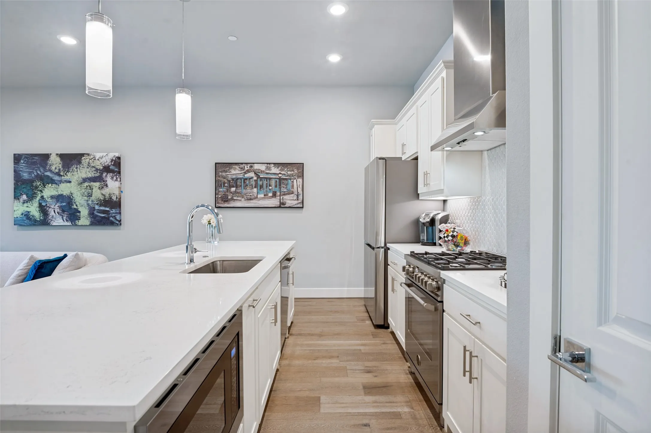 Modern kitchen featuring white cabinetry, stainless steel appliances, a large island with an undermount sink, and wood-finish flooring