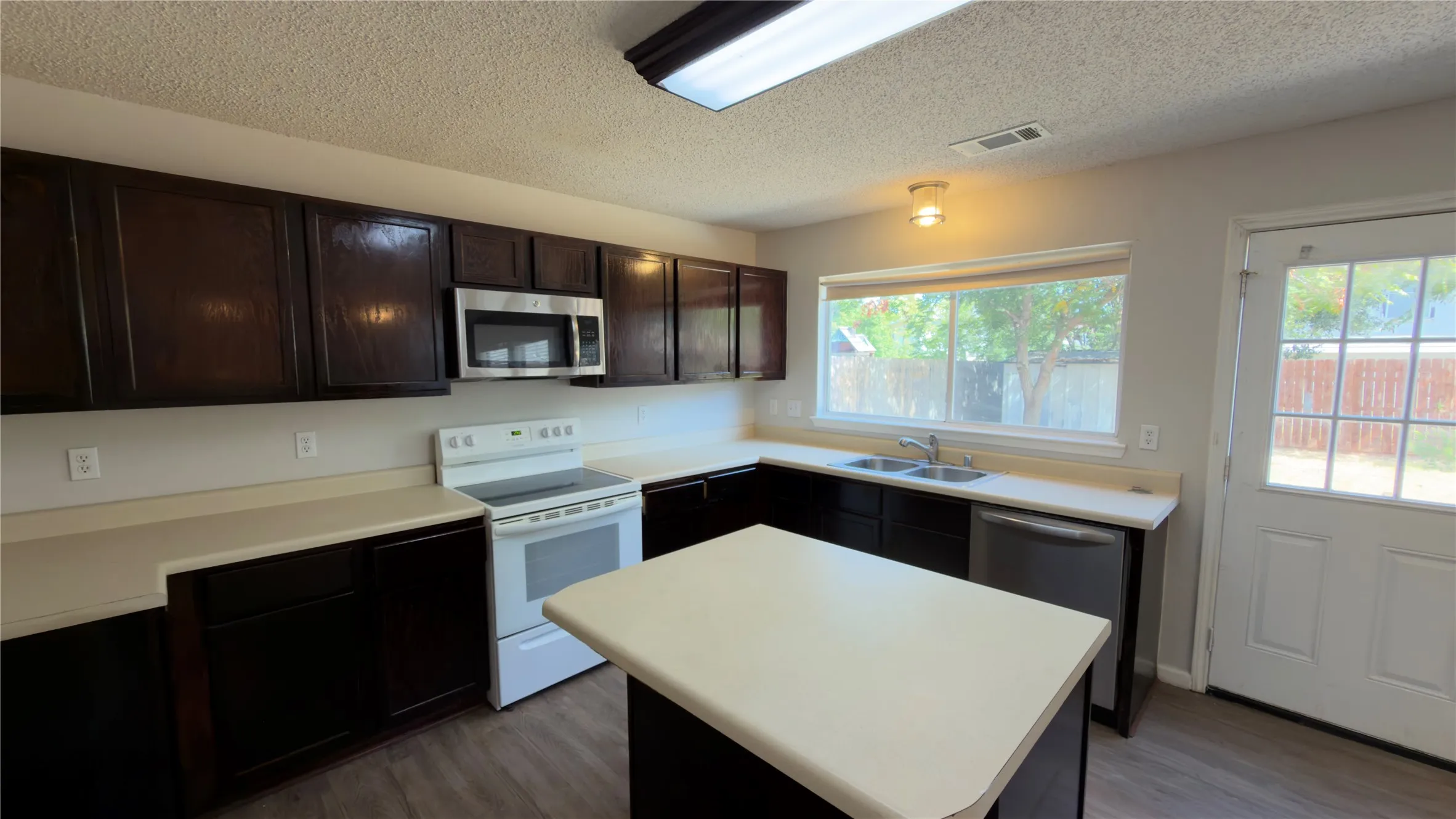 Kitchen featuring dark wood-finish cabinetry, light-toned countertops, a white electric range, and a stainless steel over-the-range microwave
