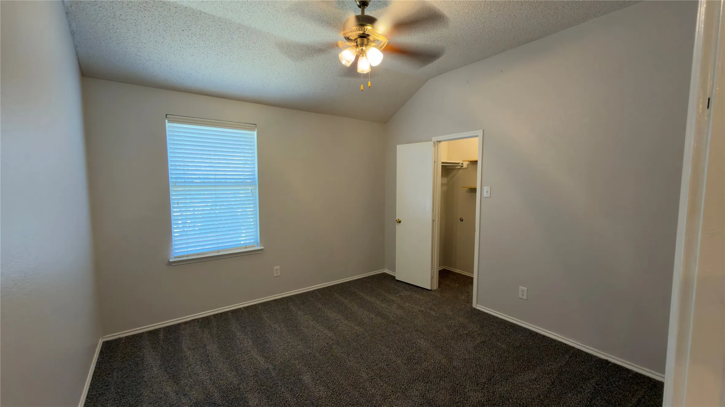 Vaulted ceiling with a ceiling fan, window with blinds, dark grey carpeting, and a closet with shelving