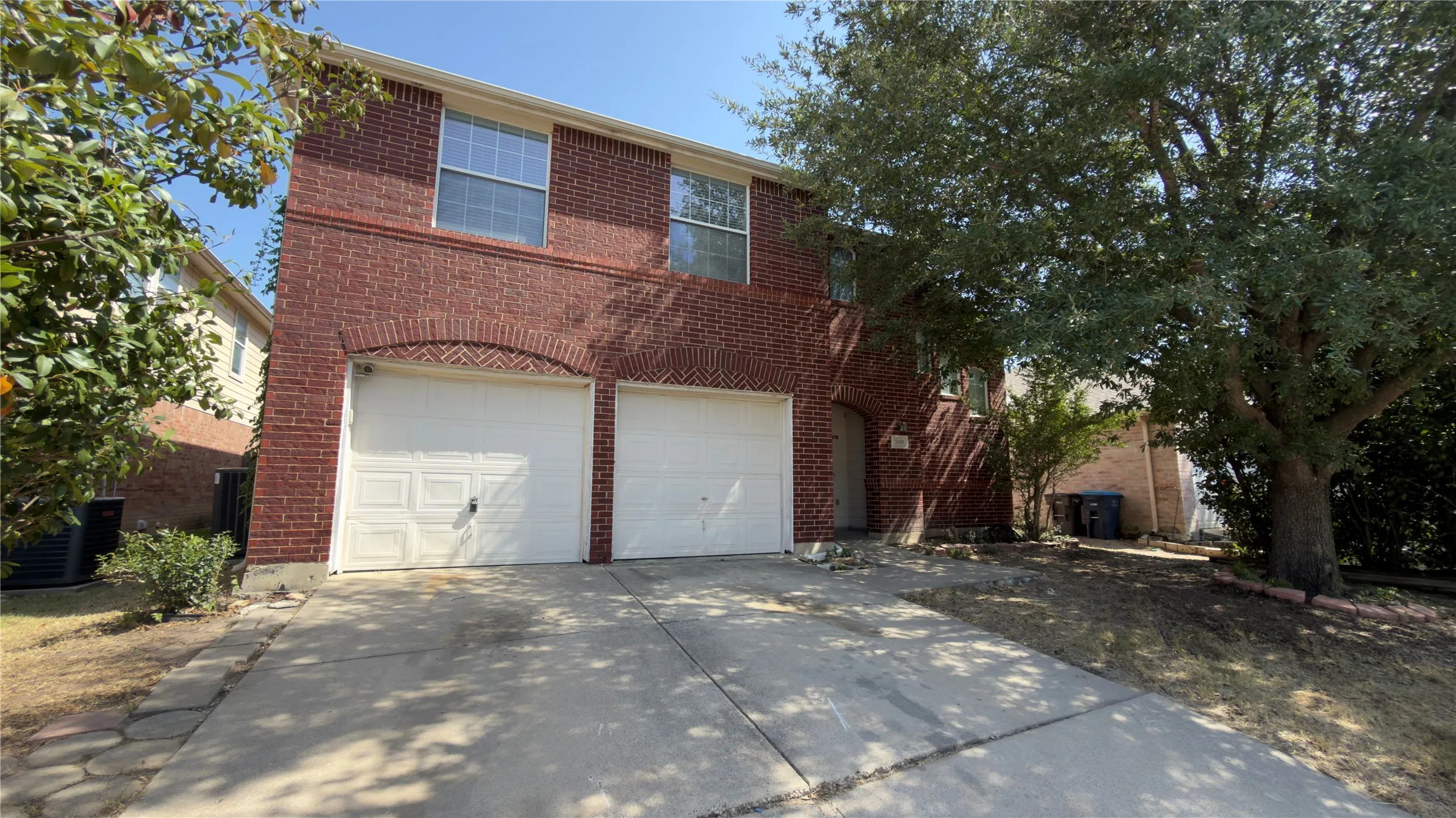 Brick exterior with arched garage door detailing, dual white garage doors, and upper-level windows
