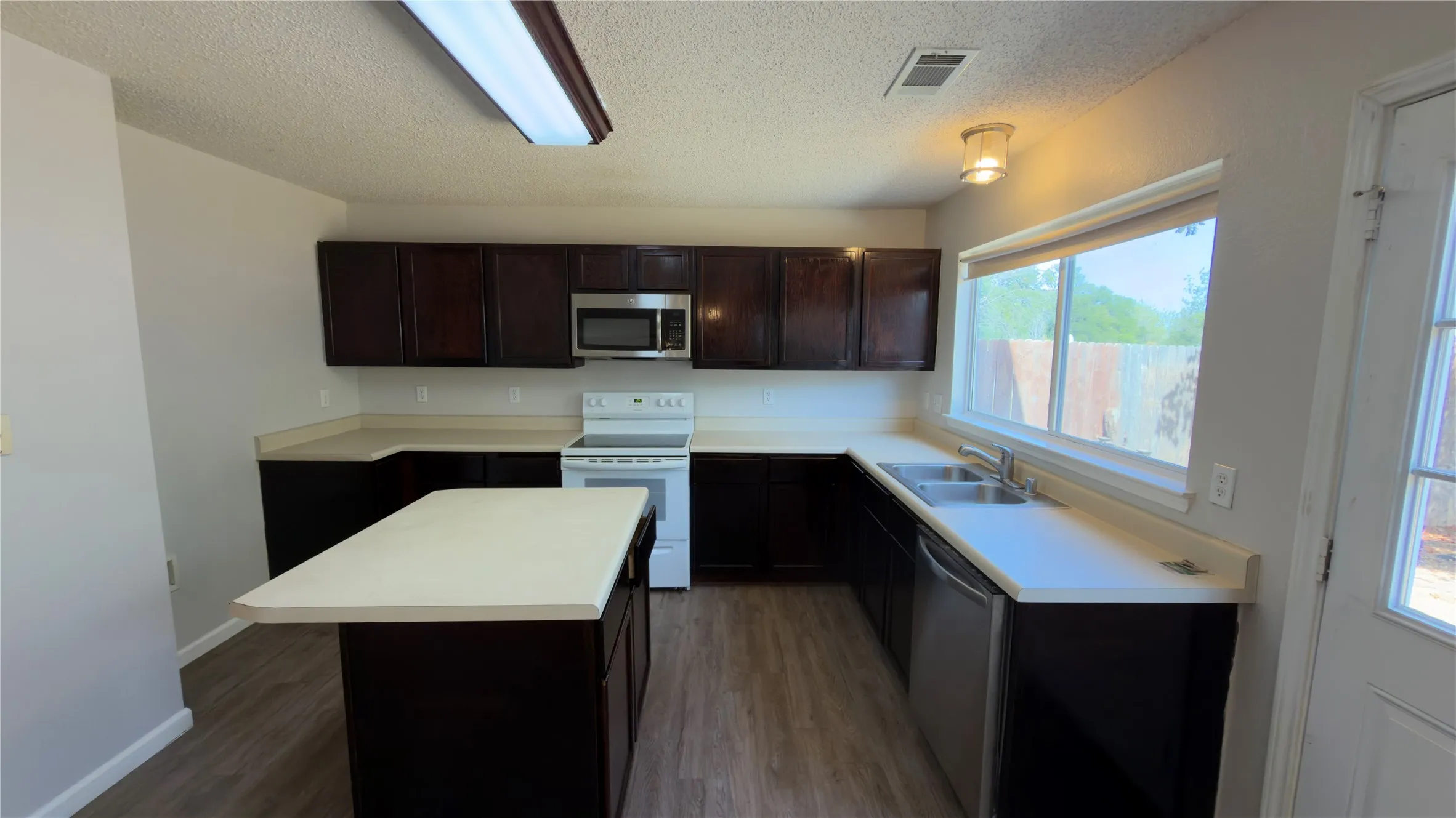 Kitchen featuring dark wood-finish cabinetry, light countertops, wood-finish flooring, a stainless steel microwave