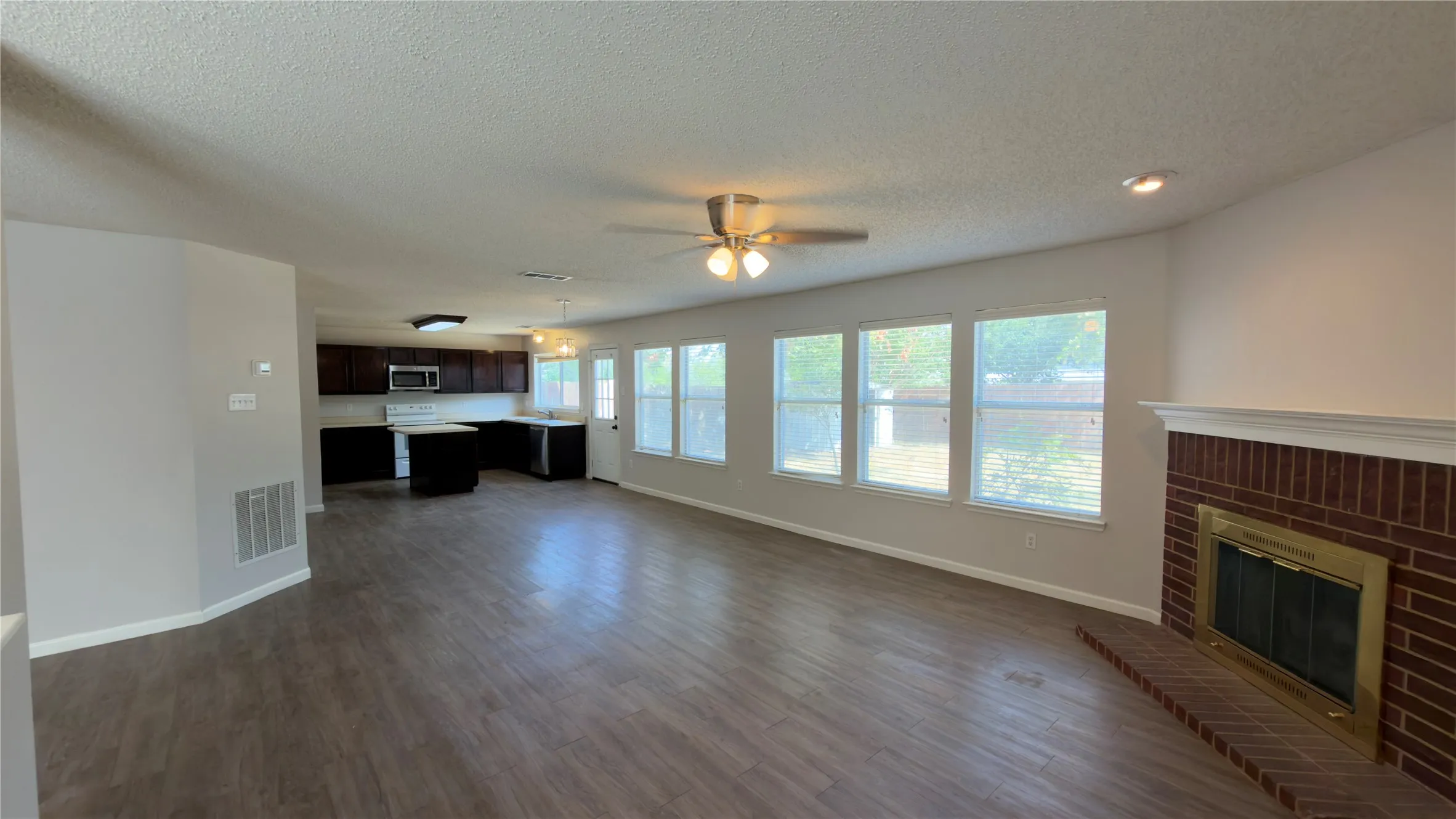 Expansive living area with wood-finish flooring, a brick fireplace, and multiple windows