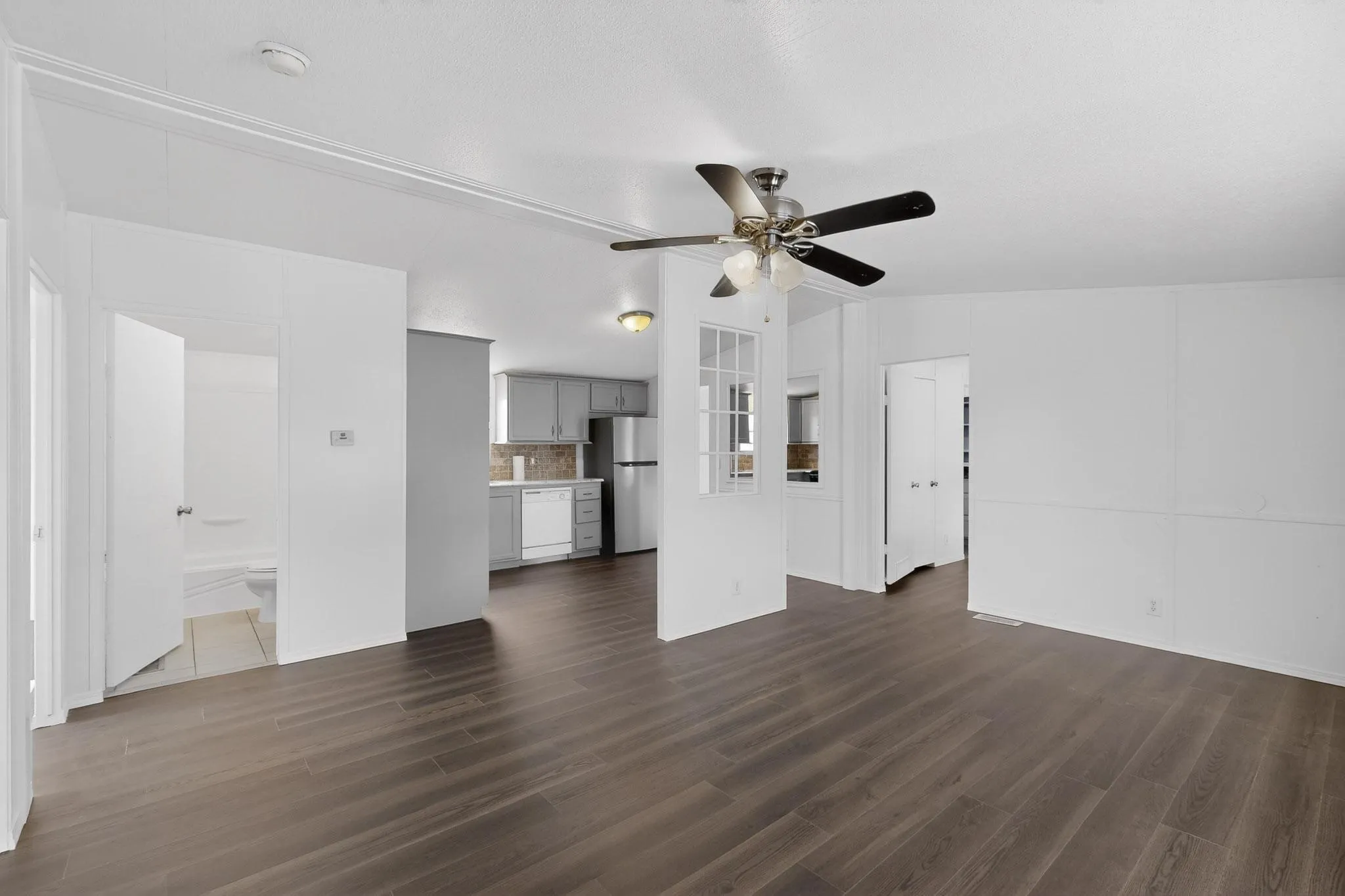 Unfurnished living room featuring ceiling fan, dark wood-style flooring, and vaulted ceiling